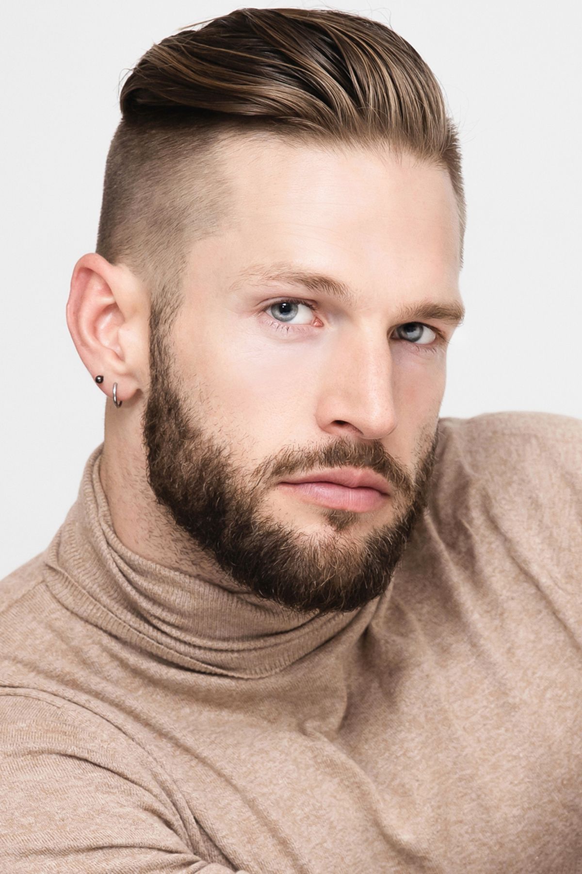 Close-up portrait of a stylish bearded man with undercut hairstyle wearing a beige turtleneck sweater.