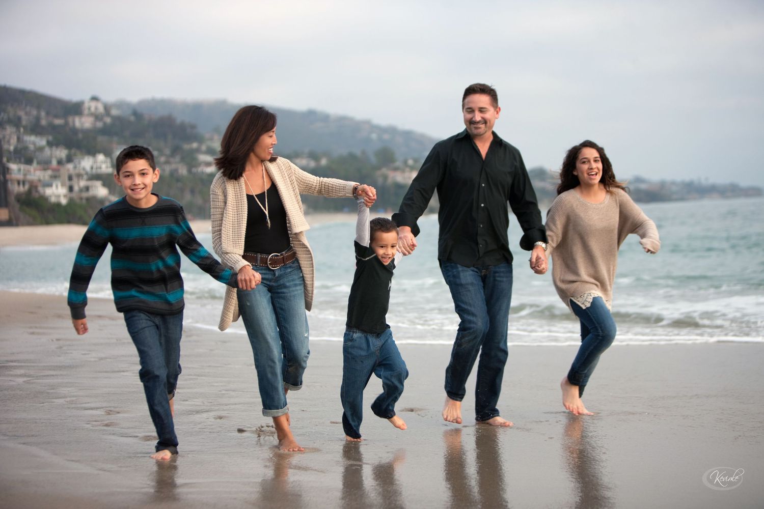 Joyful family of five holding hands walking barefoot on a sandy beach.