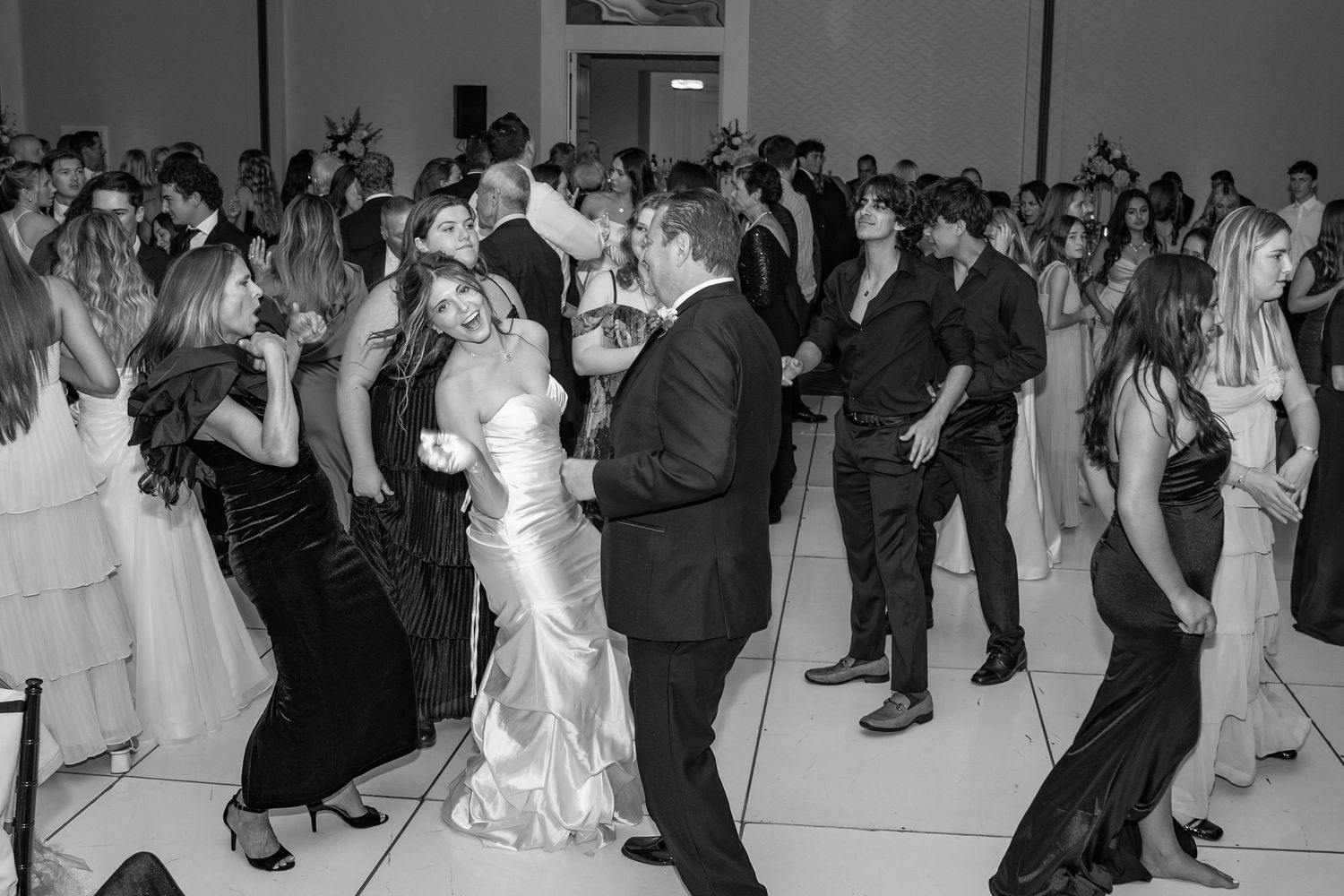 Black and white photo of wedding guests dancing joyfully at a lively wedding reception celebration.
