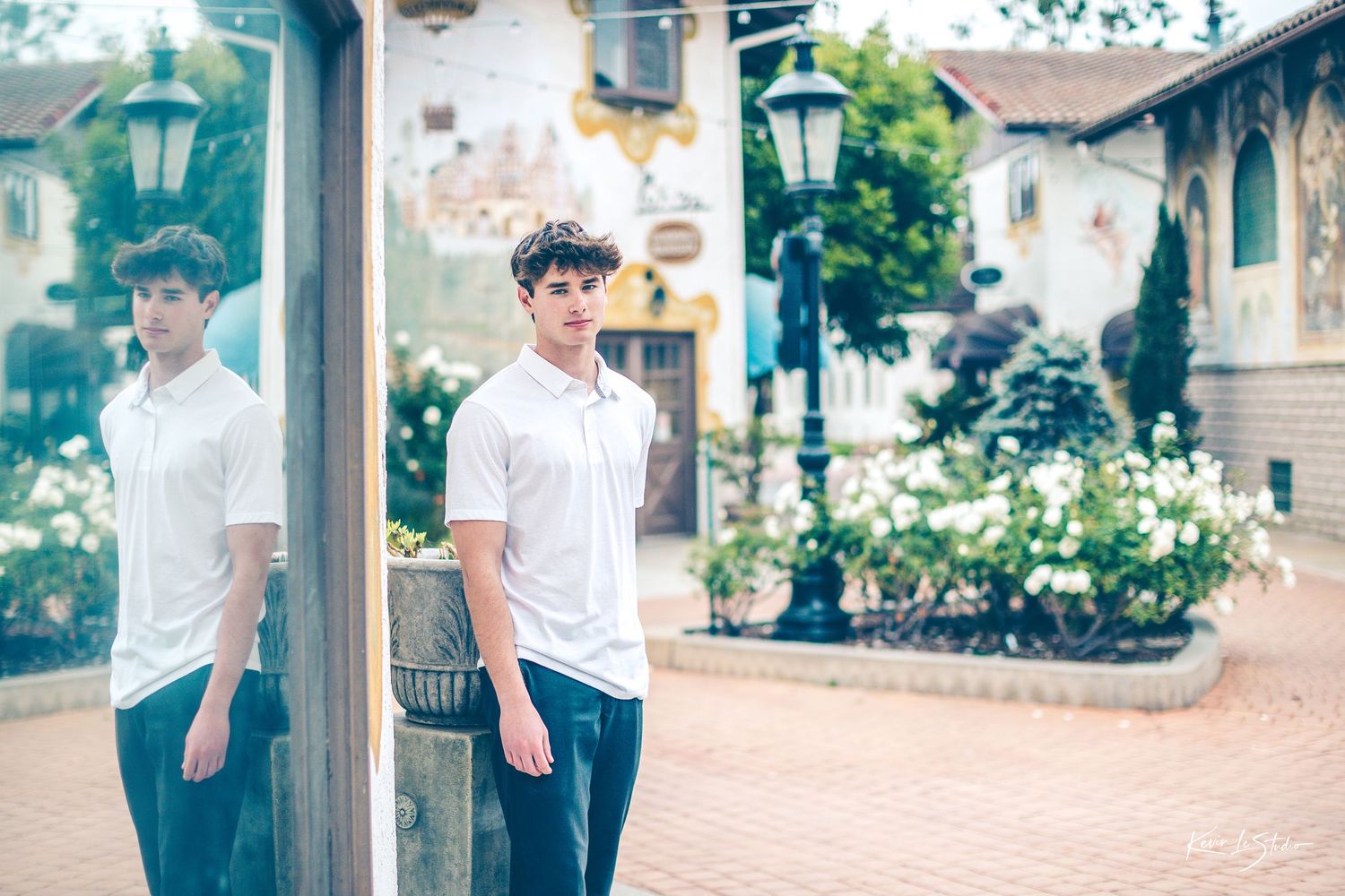 Young man in white polo shirt reflected in a mirror outdoors in a decorative European village setting.