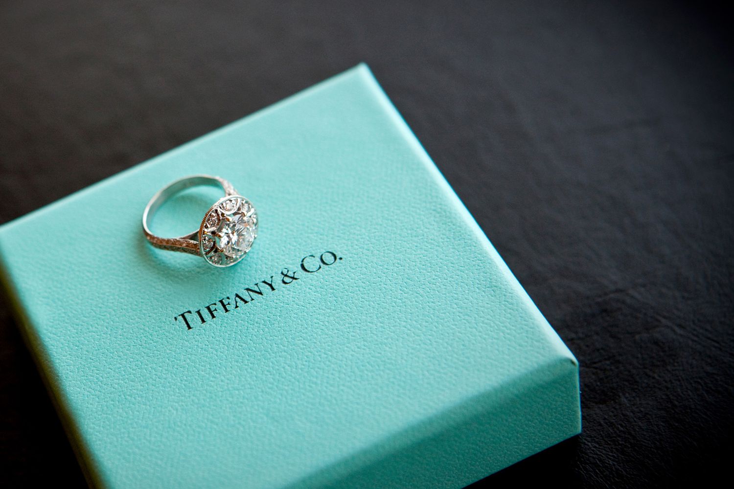Diamond cluster ring displayed on a light blue Tiffany and Co. gift box on dark surface.