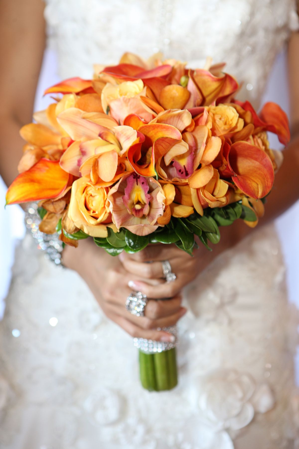 Bride holding vibrant orange and red calla lily and rose wedding bouquet with jeweled bracelet.