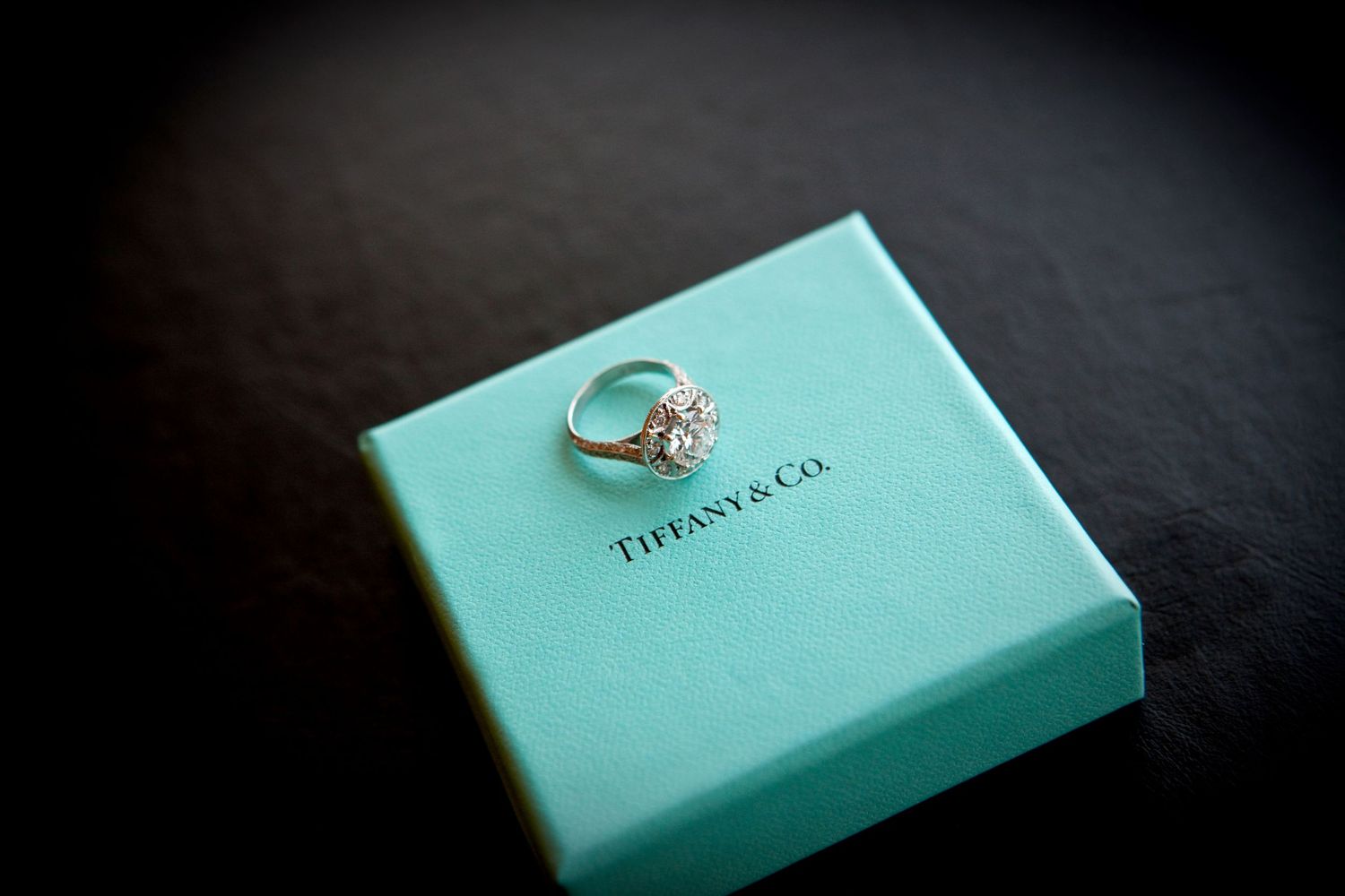 A sparkling diamond ring displayed on a Tiffany & Co. signature blue gift box on a dark background.