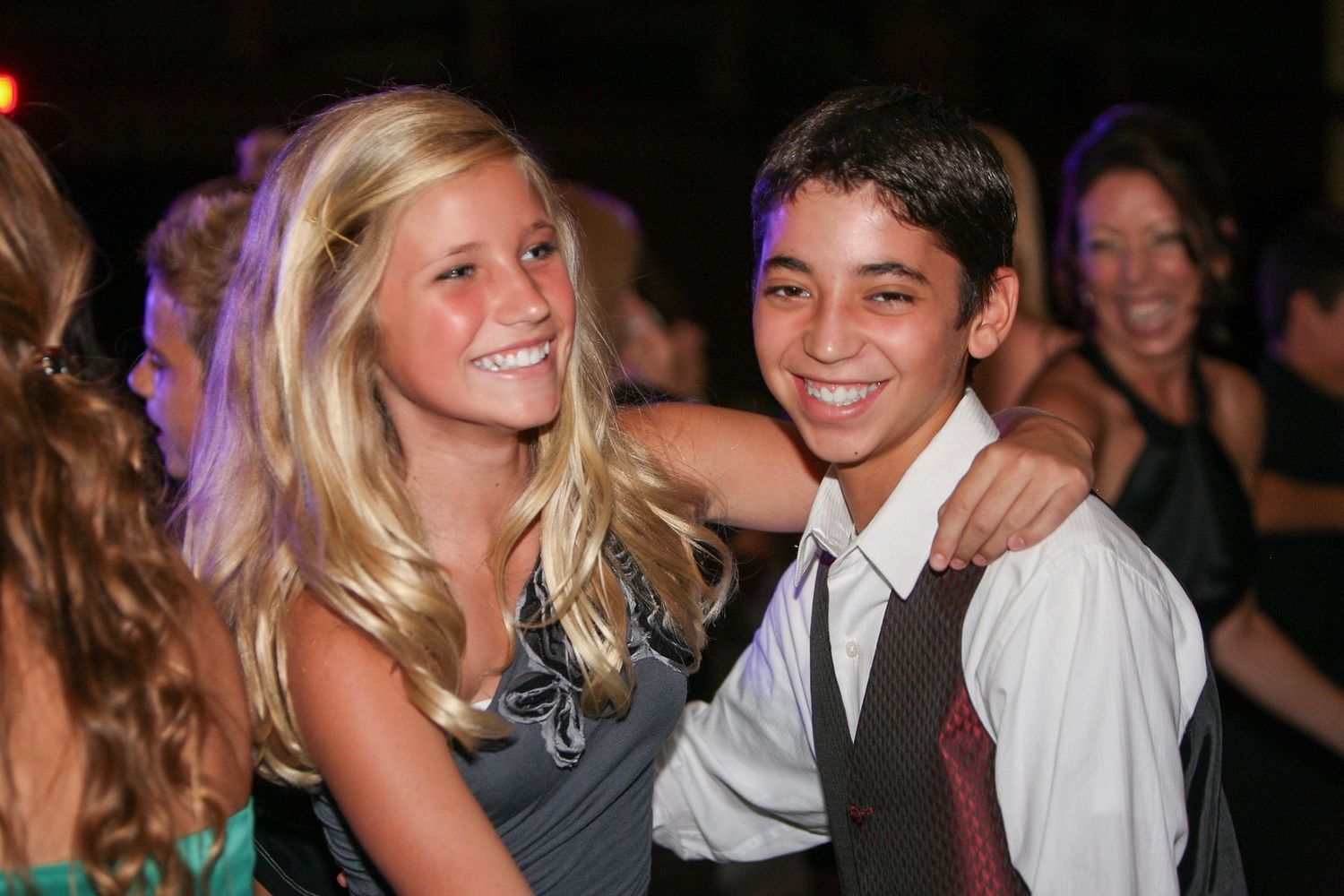 Two smiling teenagers pose together at a formal dance event, boy in tie and girl in evening wear.
