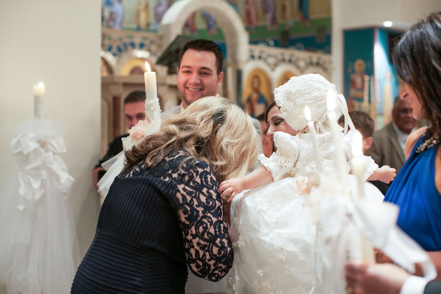 Orthodox baptism ceremony with guests in white garments holding candles inside a decorated church.