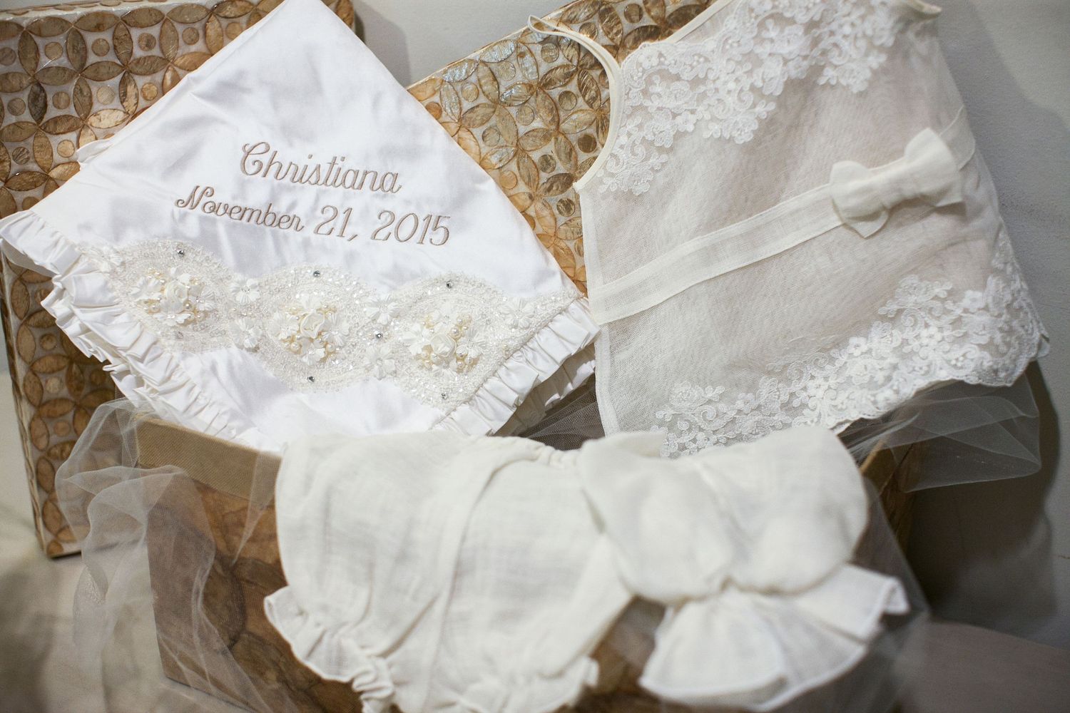 White lace christening set with embroidered pillow reading Christiana December 21, 2015, gown, and bonnet in basket.