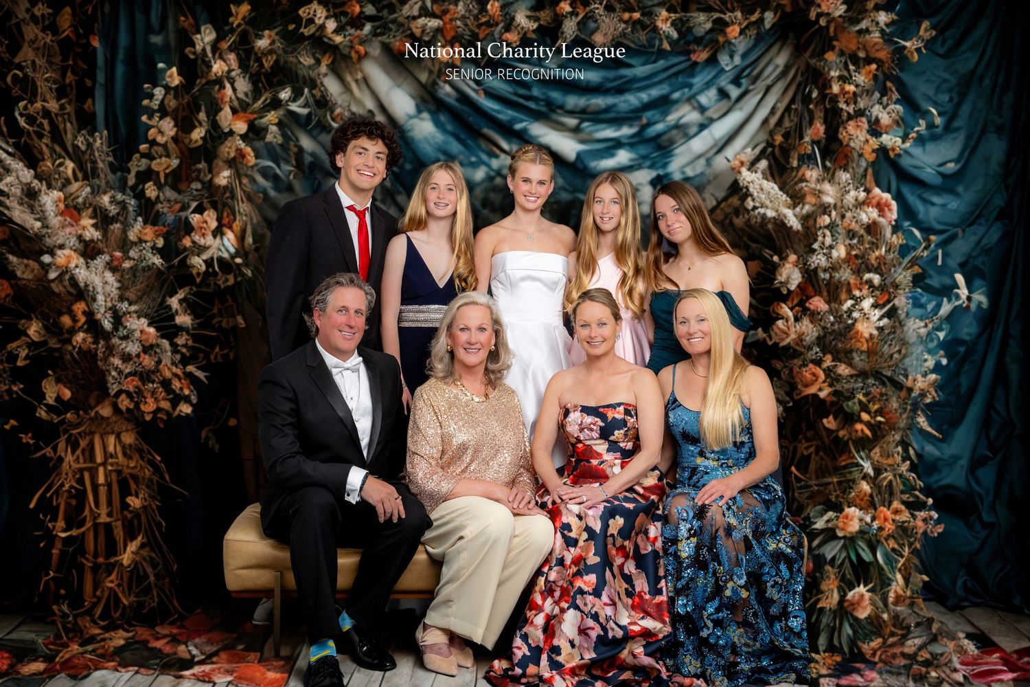 Family group portrait at National Charity League formal event, posed in front of floral backdrop, dressed in elegant attire.
