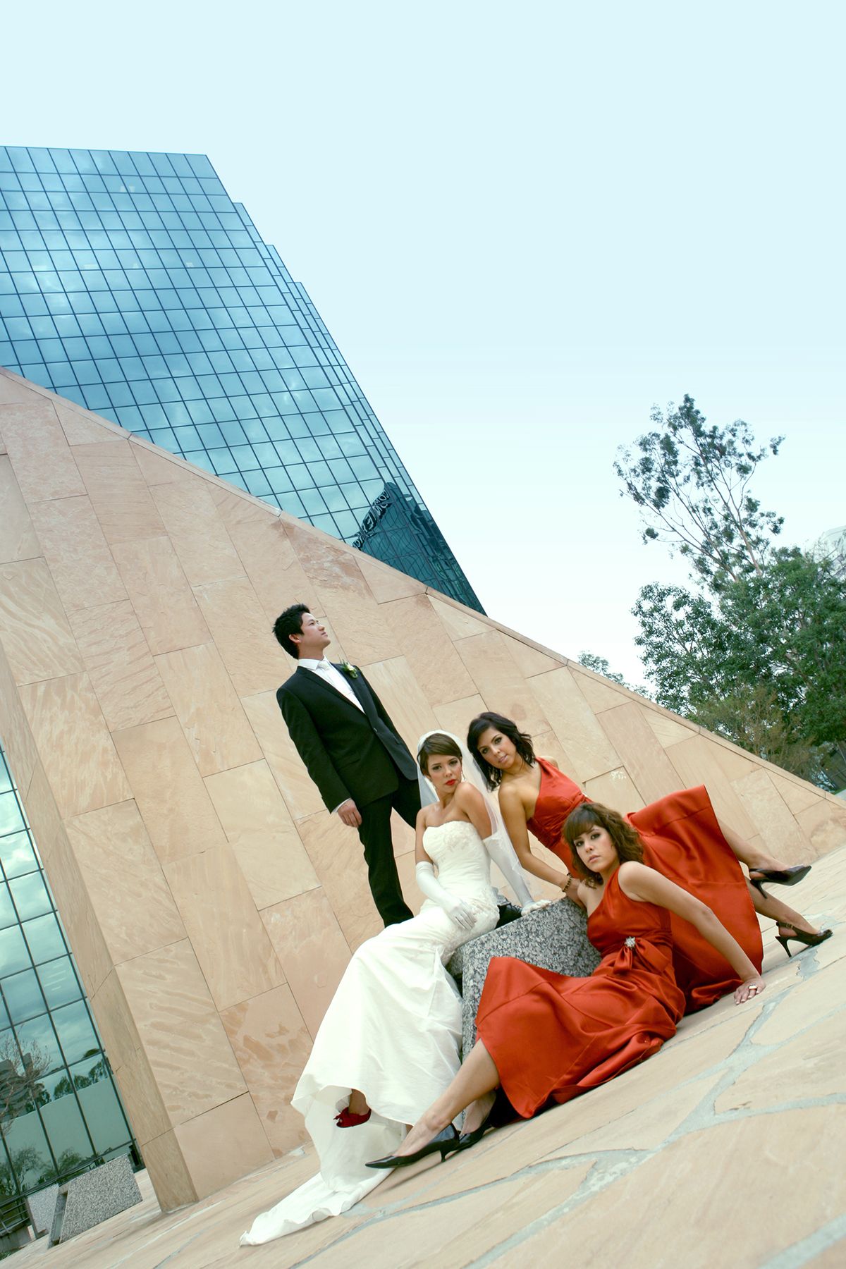 Wedding party with bride in white gown and bridesmaids in red dresses posing near a modern building.