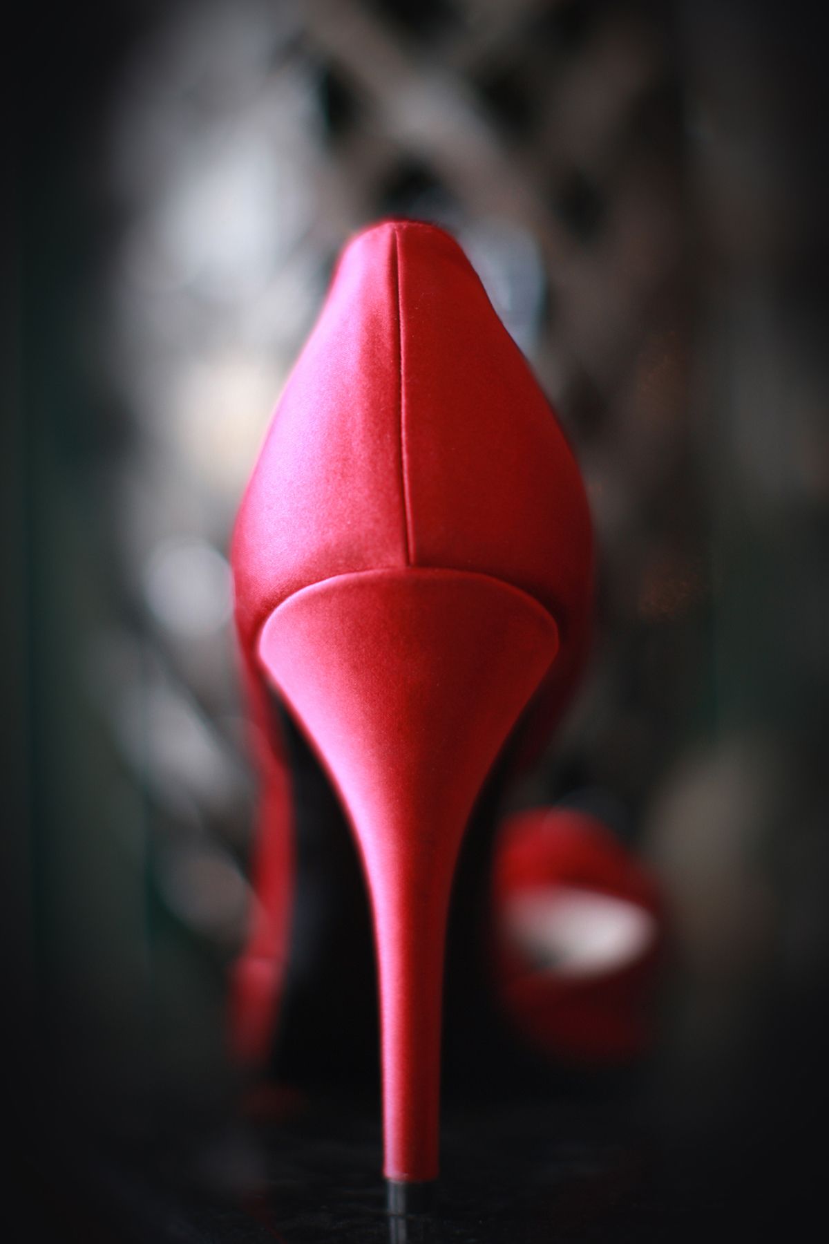 Close-up rear view of a vibrant red satin stiletto high heel shoe with blurred background.