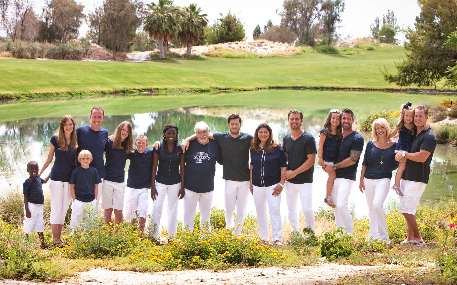 Large family group posing in matching navy and white outfits on a lush golf course beside a scenic pond.