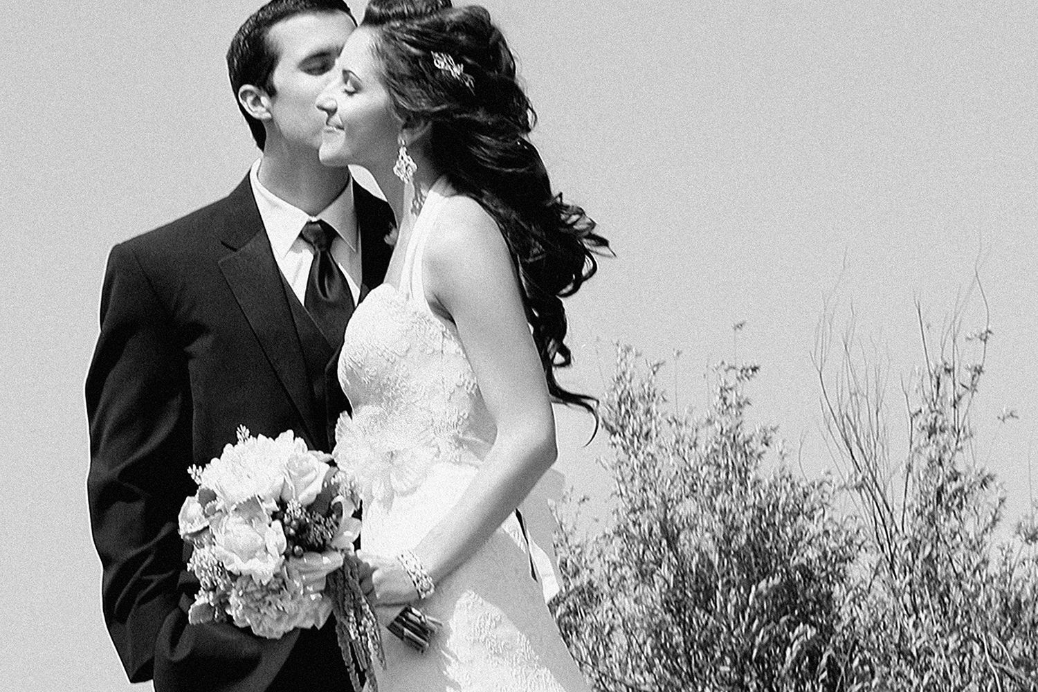 Bride and groom kissing outdoors in a classic black and white wedding photo.