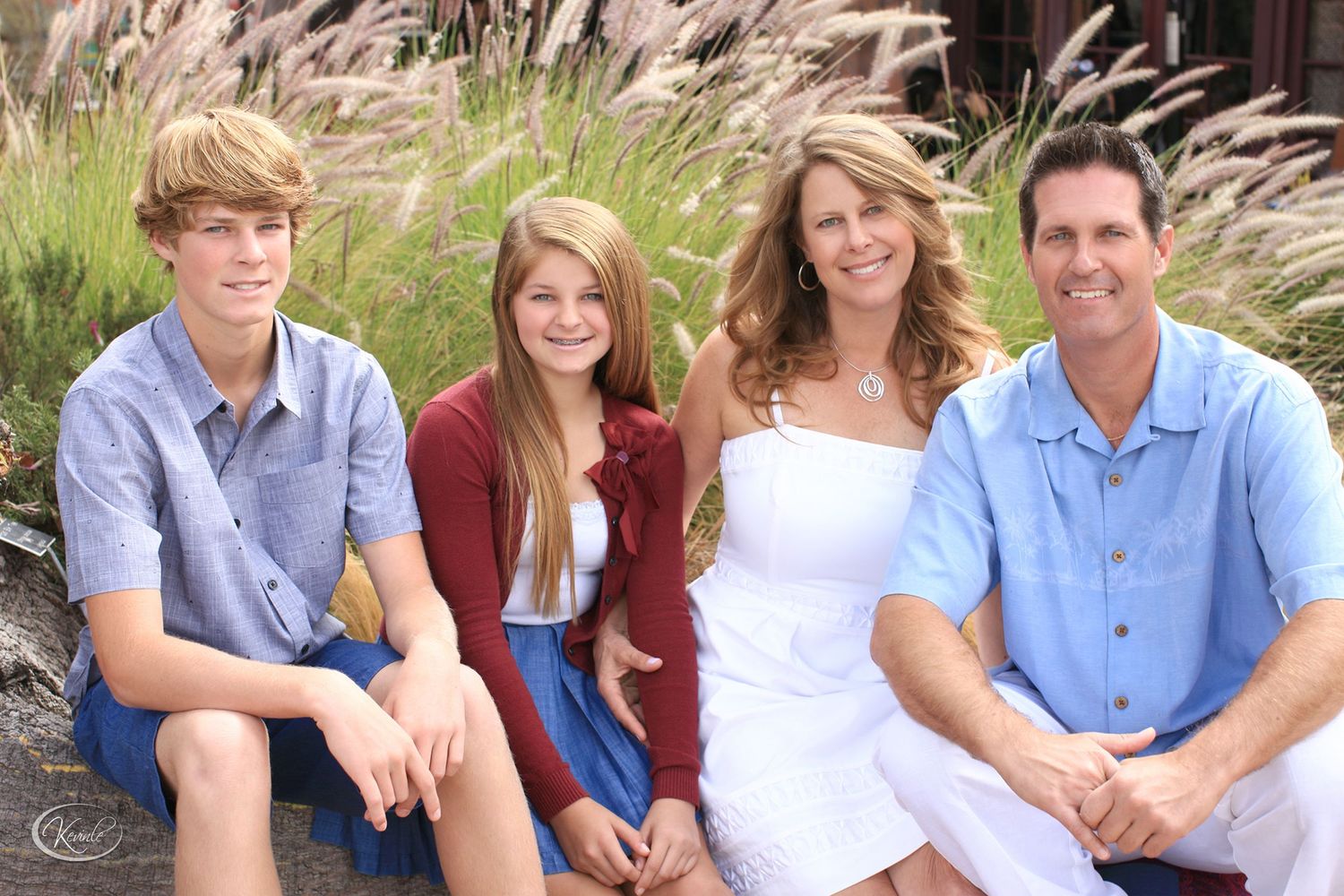 Happy family of four smiling together outdoors near natural grasses.