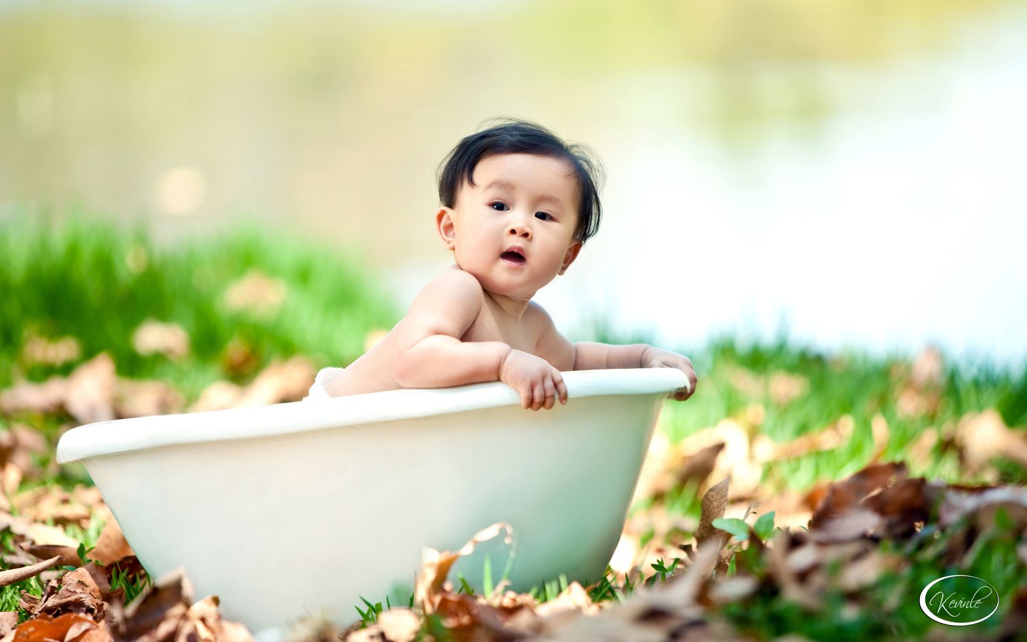 Cute Asian baby sitting in a white bathtub outdoors surrounded by autumn leaves.