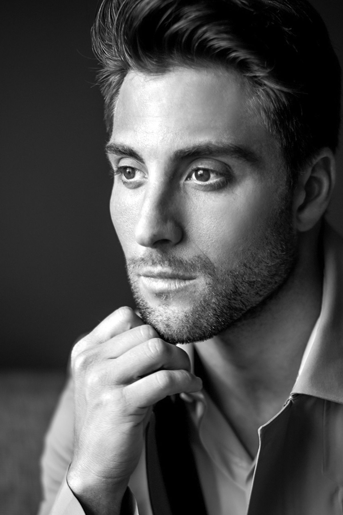 Black and white portrait of a handsome young man with stubble holding his tie, looking thoughtfully at camera.