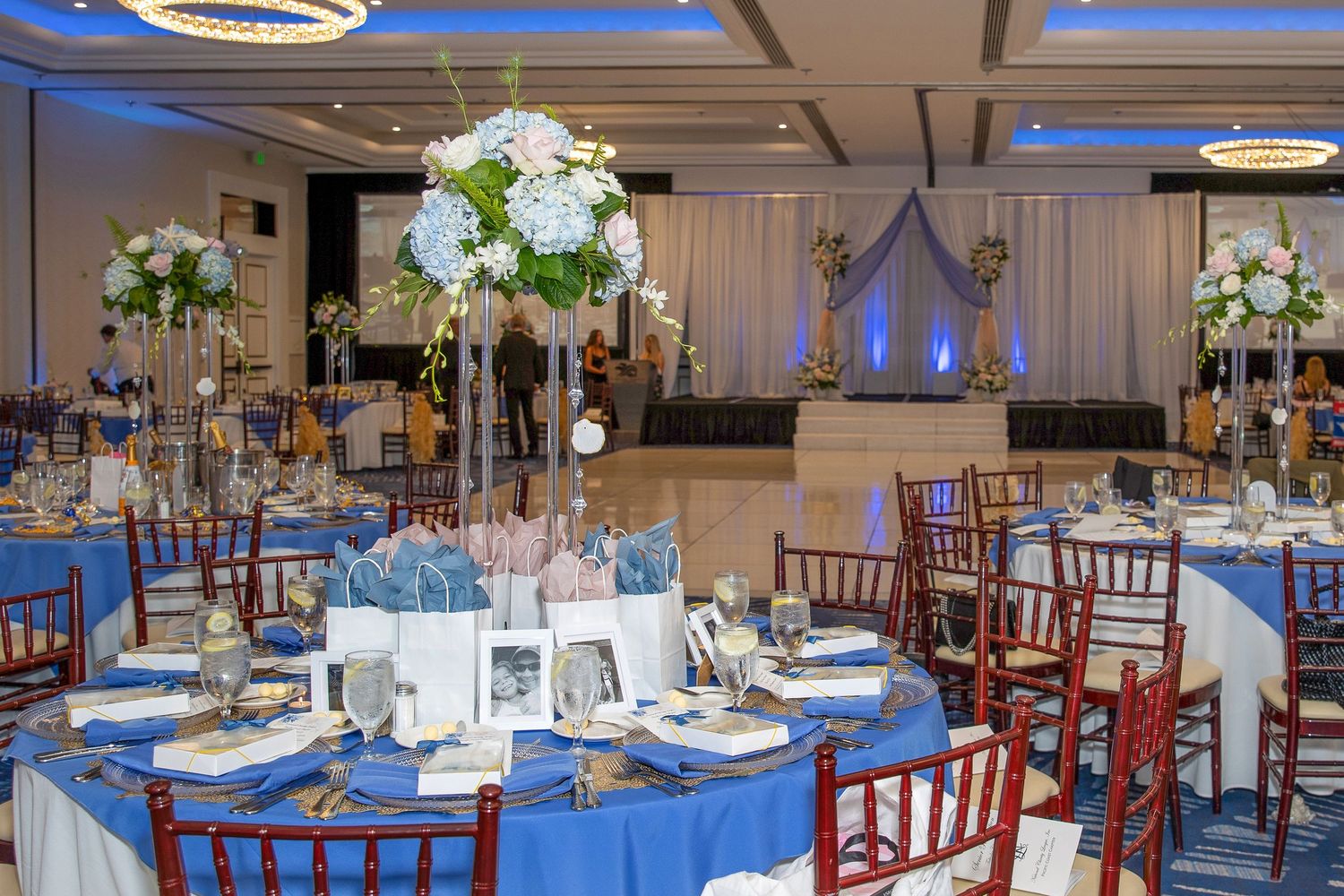 Elegant banquet hall with blue tablecloths, tall floral centerpieces, and chiavari chairs set for a formal event.