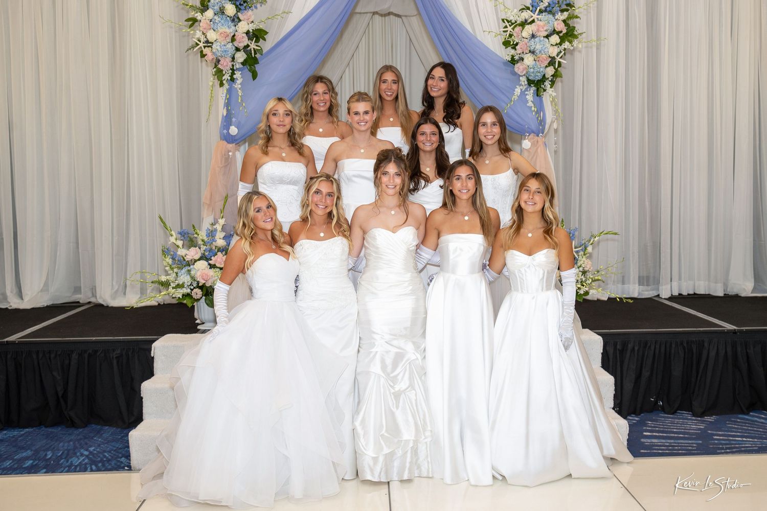 Group of young women in elegant white ball gowns posing together at a formal debutante ball event.