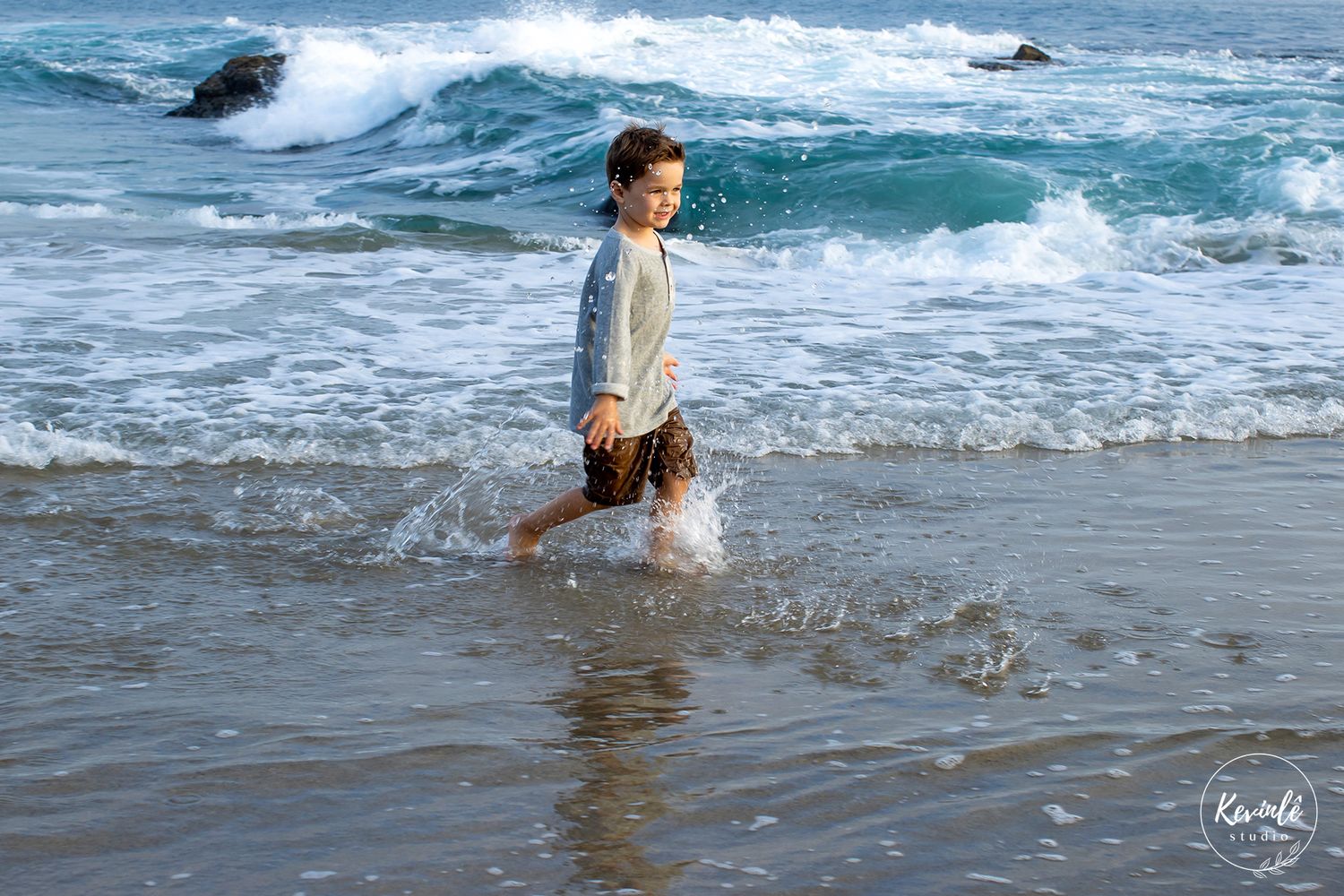 A child joyfully splashing through ocean waves on a sunny beach day.