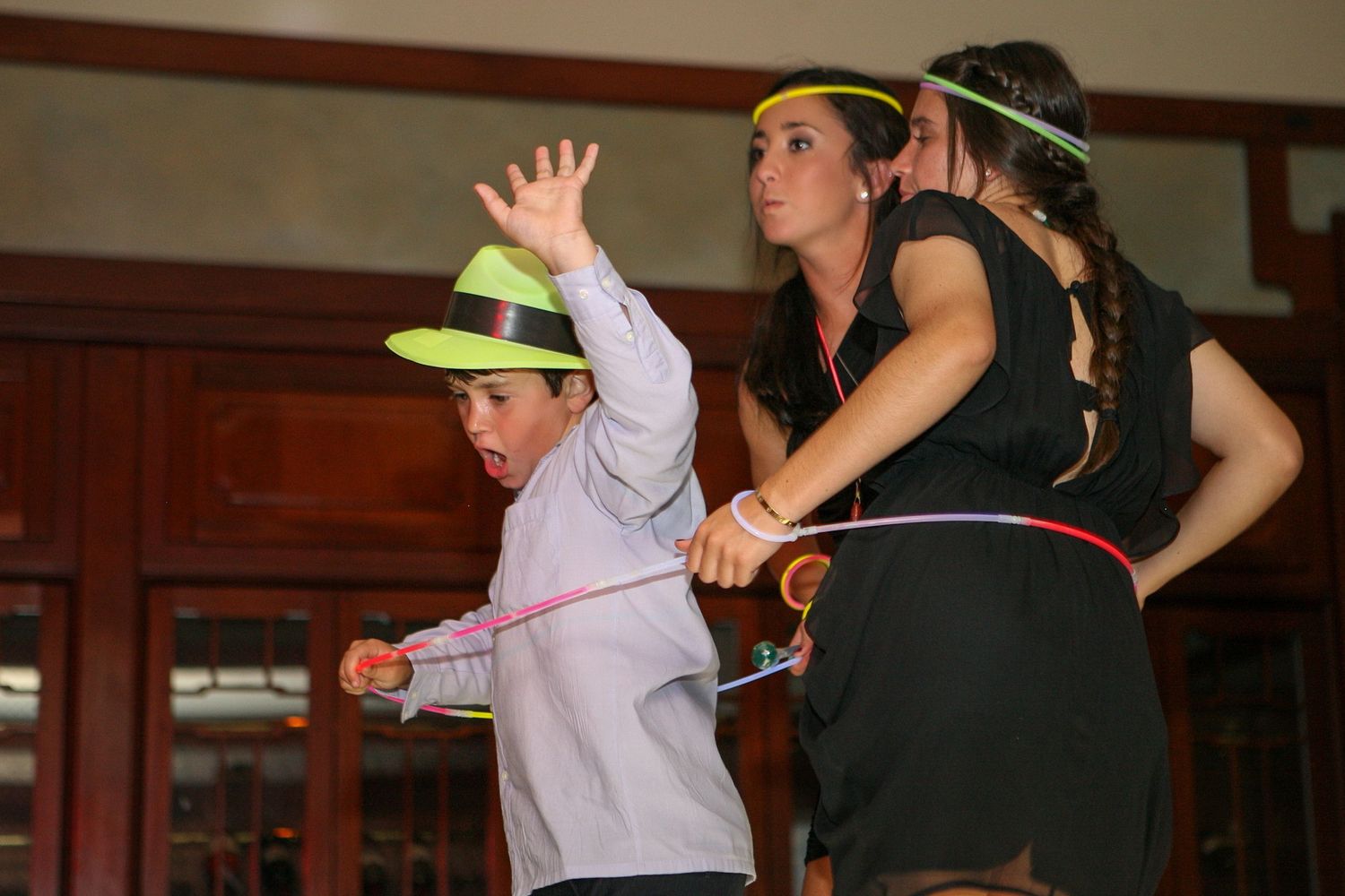 Children and adults hula hooping with colorful glow sticks at a festive indoor party event.