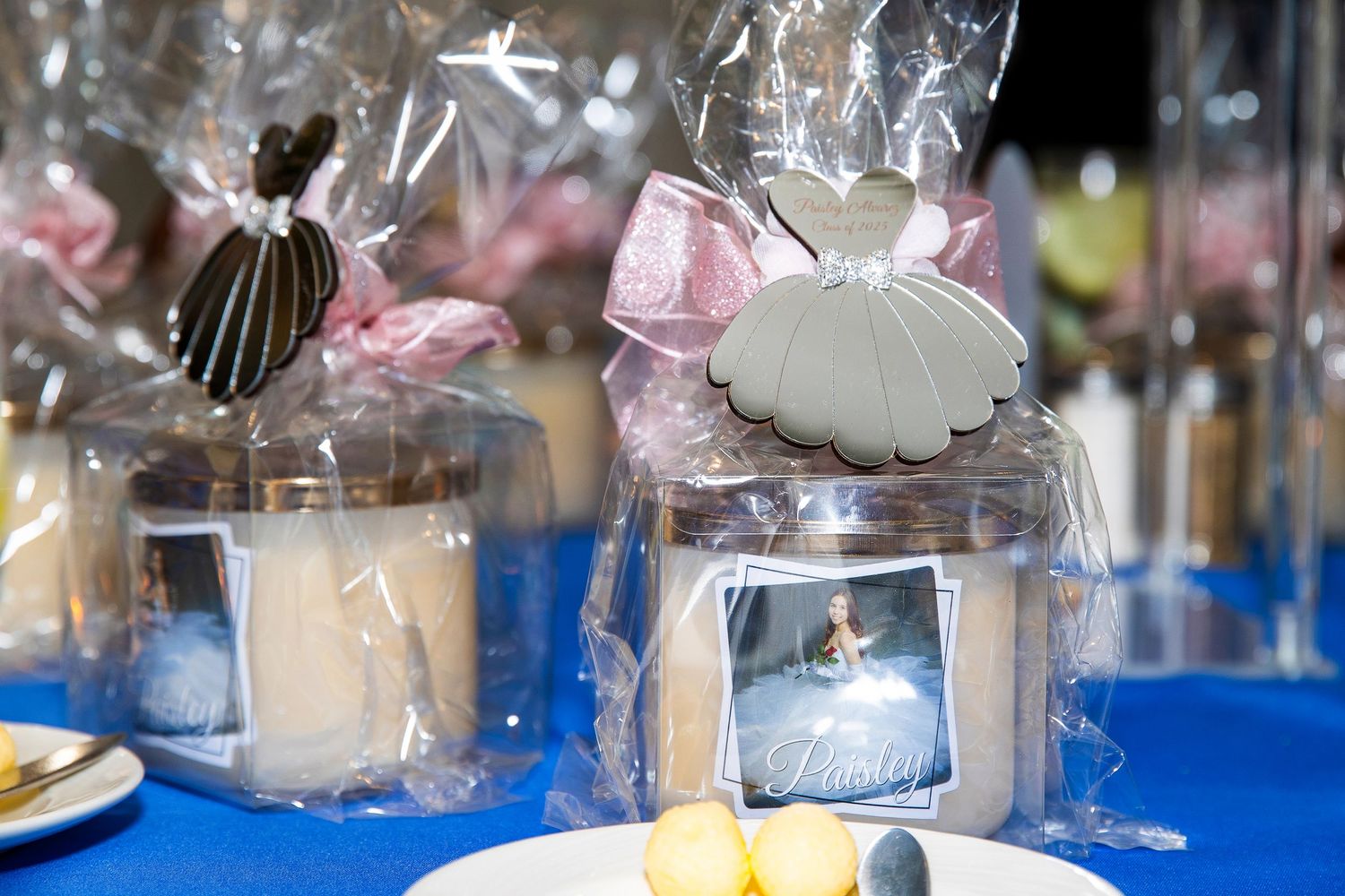 Elegant party favor bags with dress-shaped cookies and candles on a blue tablecloth at a celebration event.