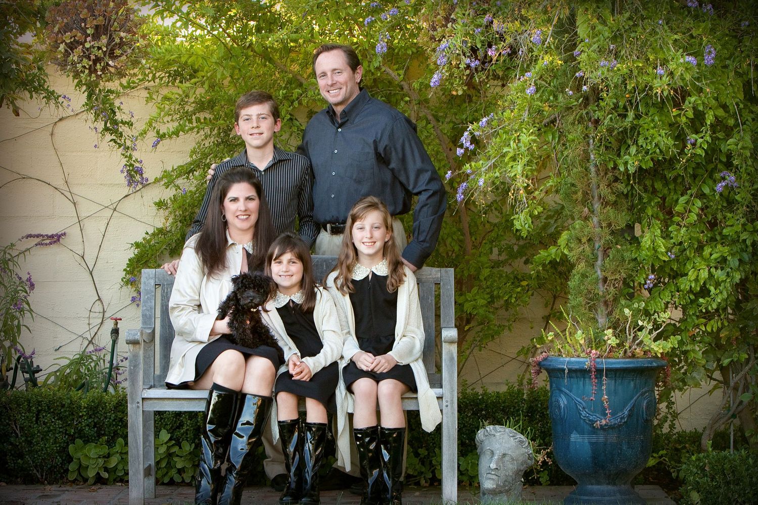 Family of five posing outdoors on a bench surrounded by lush greenery for a professional portrait photo.