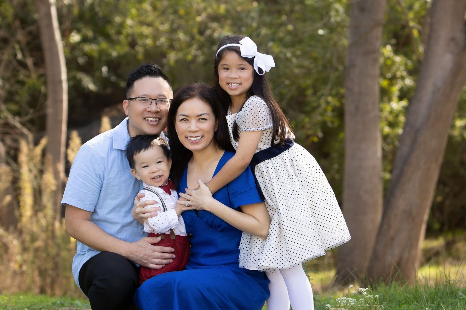 Happy Asian family of four smiling outdoors in a park, parents with young daughter and baby son.
