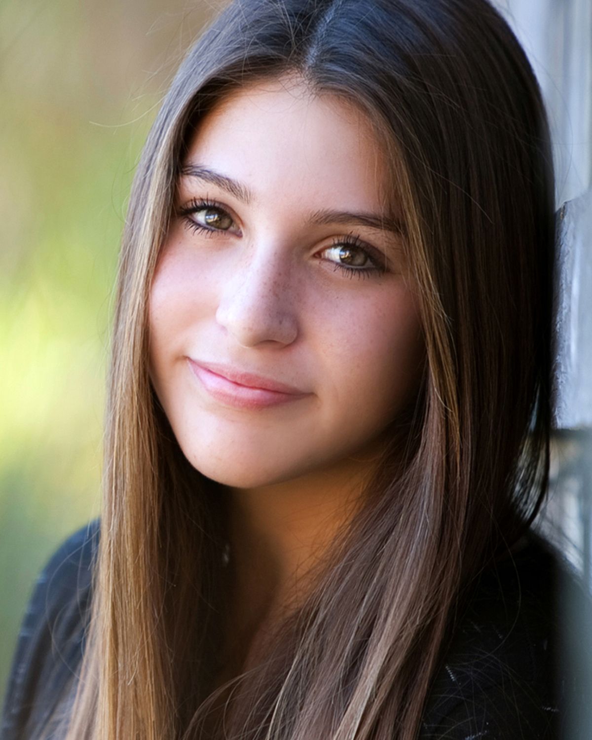 Young brunette woman with long straight hair and green eyes smiling softly in a professional headshot photo.