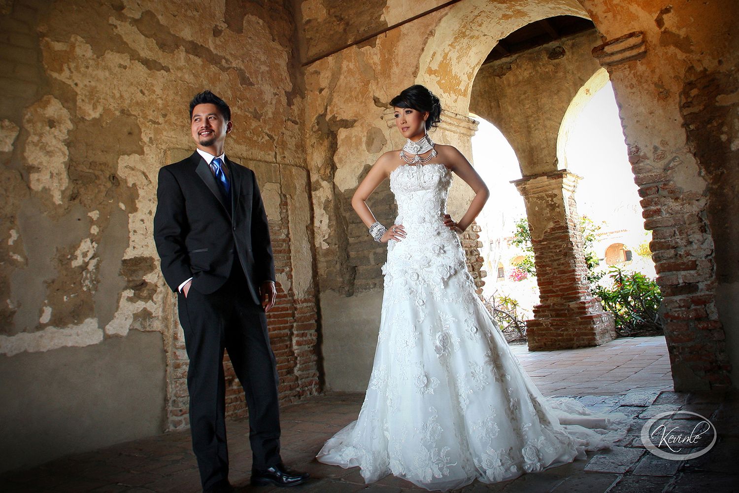 Bride and groom posing elegantly under stone arches at a historic wedding venue with rustic walls.