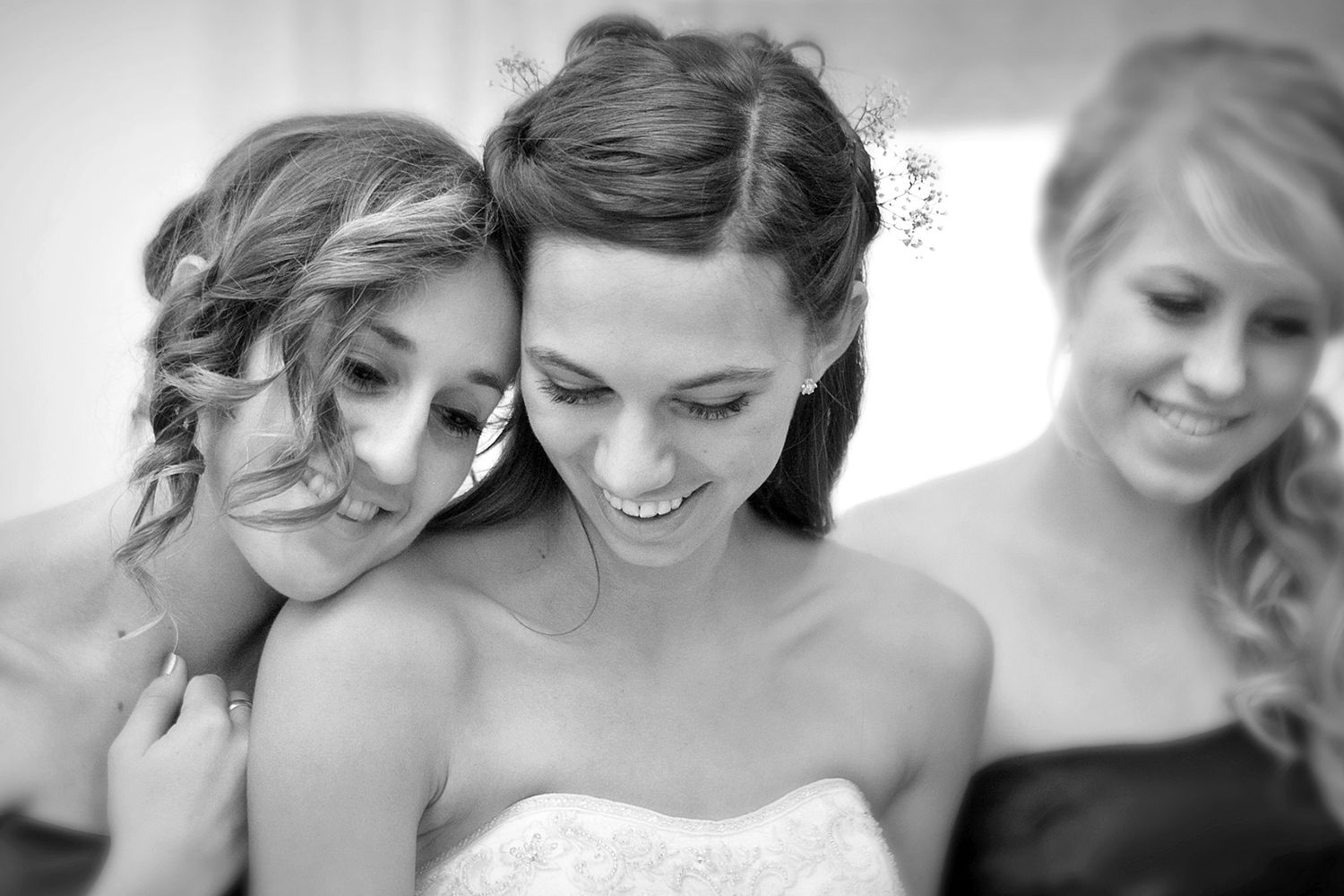 Black and white photo of a smiling bride with two bridesmaids in an intimate moment.