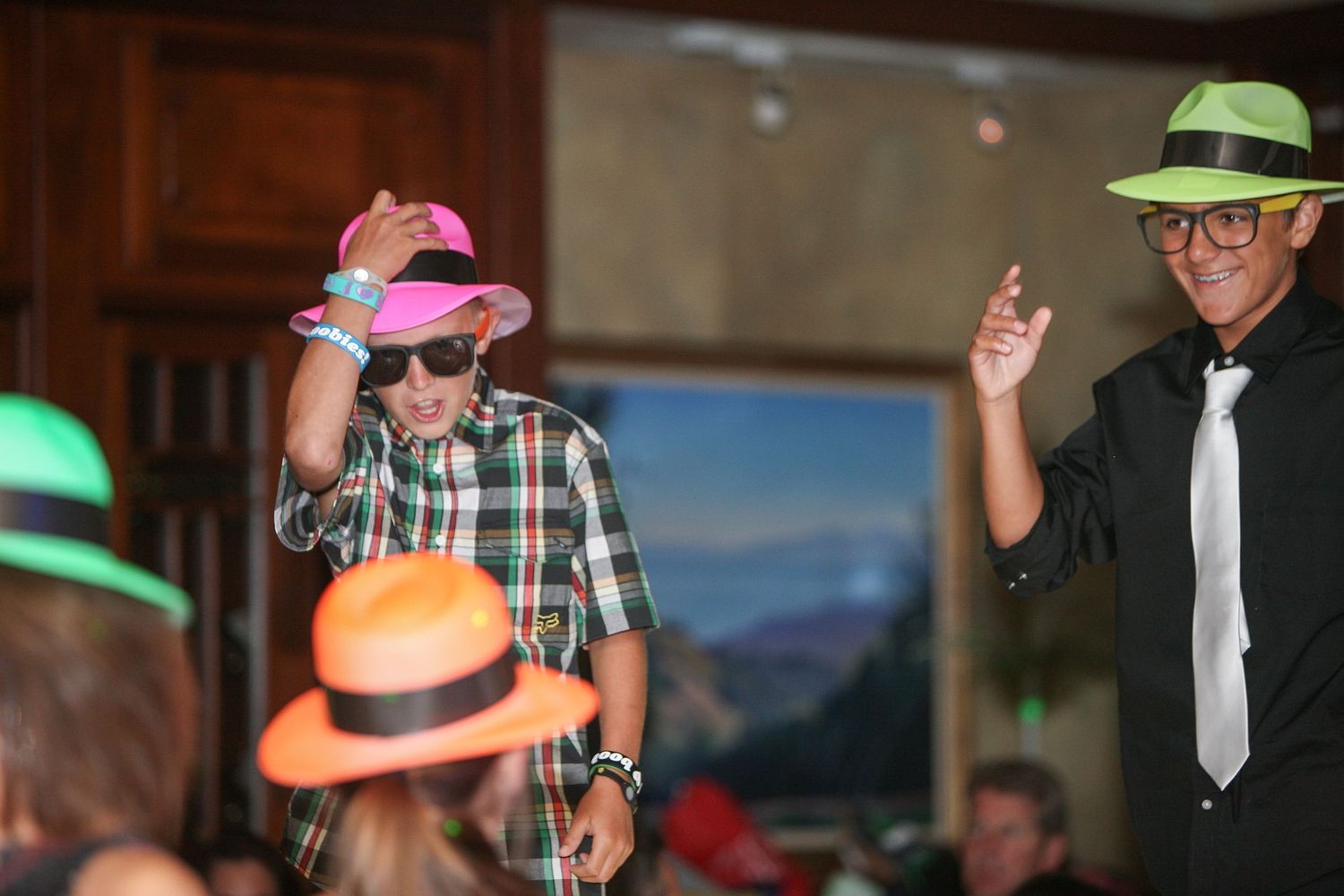 People wearing colorful neon hats dancing and celebrating at an indoor party event.