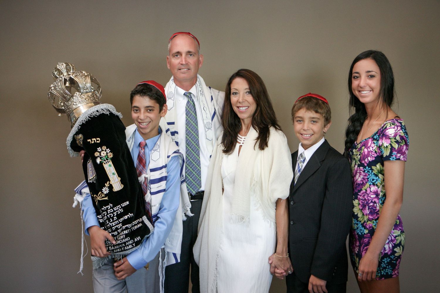 Family posing together at a Bar Mitzvah celebration, holding a Torah scroll, dressed in formal attire.