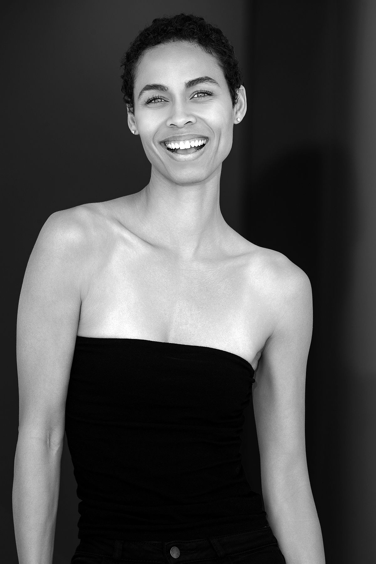 Black and white portrait of a smiling woman with short hair wearing a strapless black top.