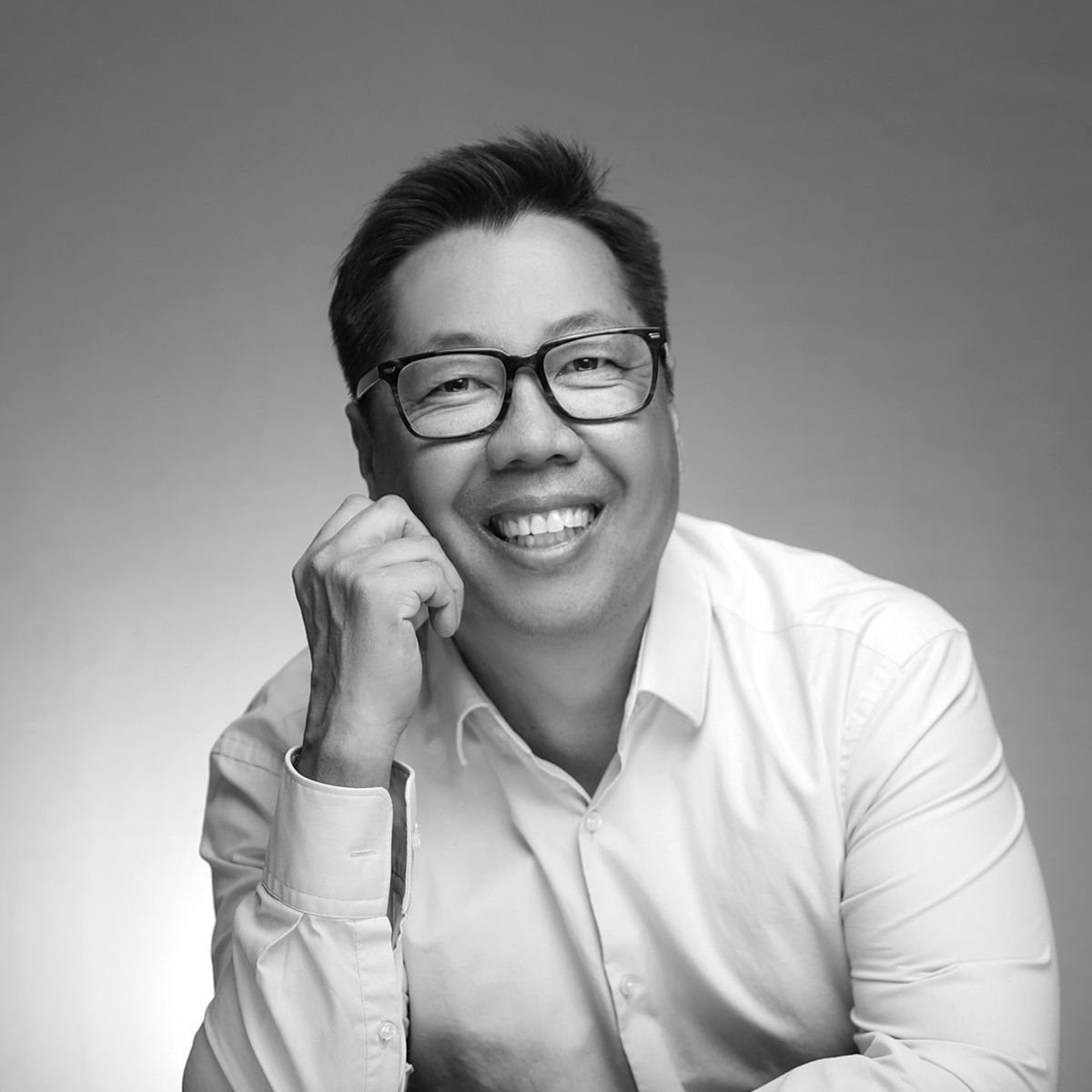Smiling Asian man in white shirt posing confidently in a black and white professional portrait photo.