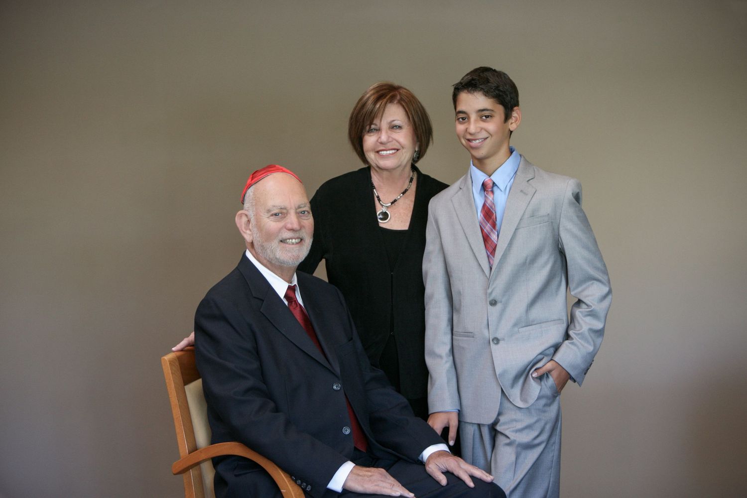 Family portrait of two adults and a teenage boy in formal attire posing together in a studio setting.