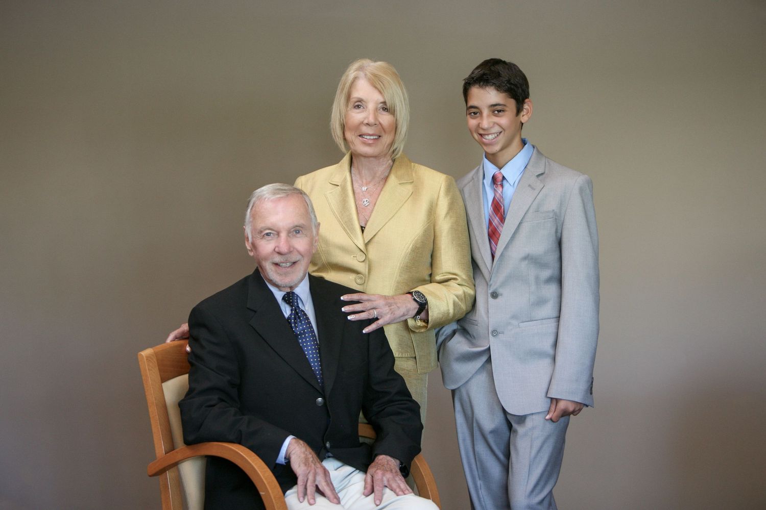 Family portrait of two older adults and a teenage boy in formal attire posing together in a studio setting.