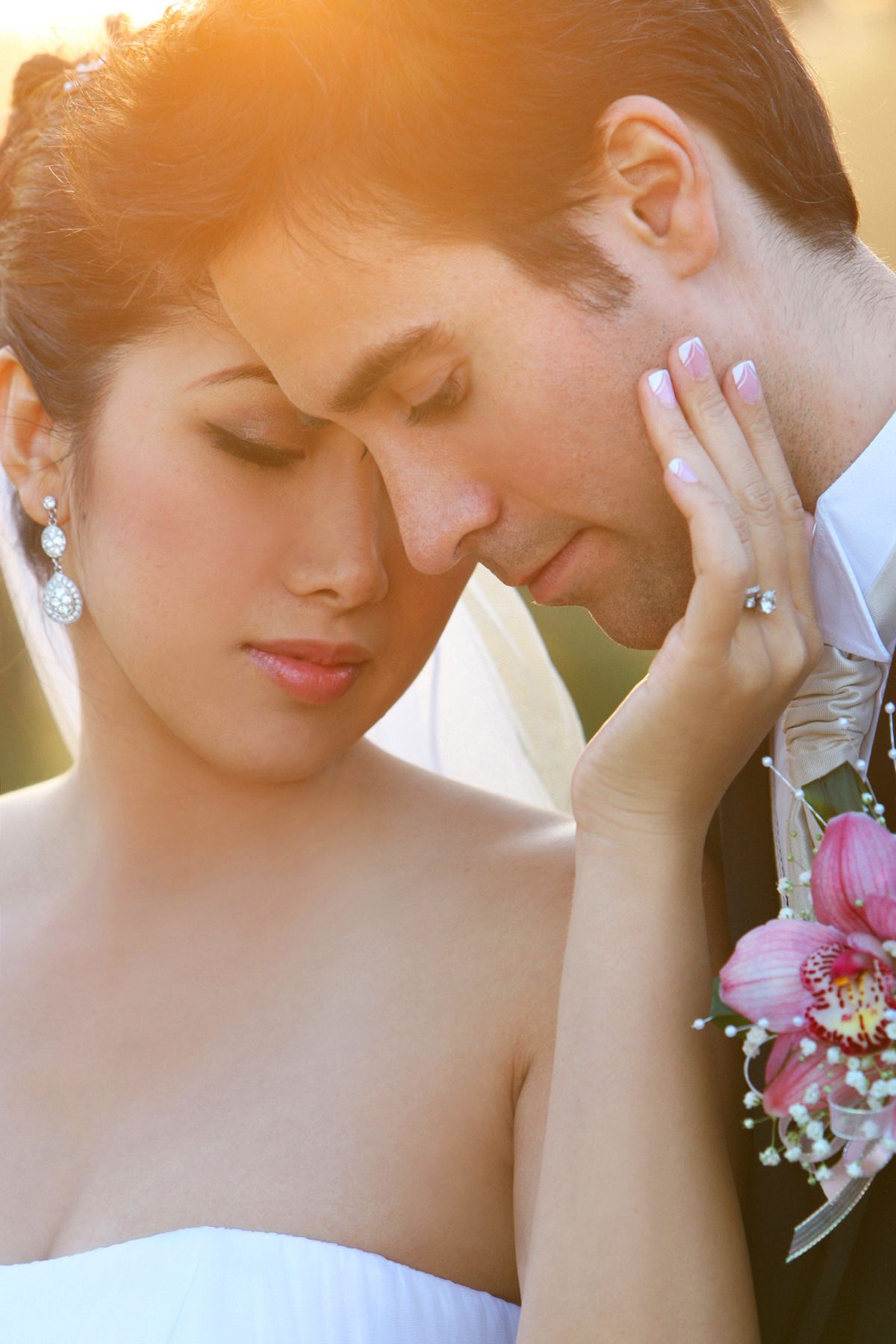 A bride and groom share an intimate moment, with the bride wearing a diamond ring and earrings in warm golden light.