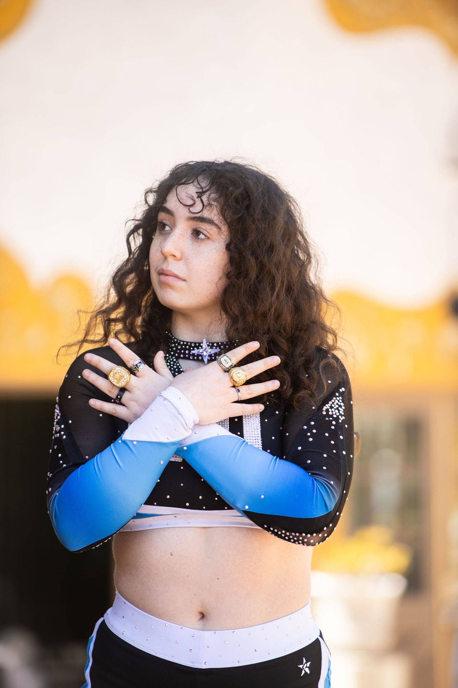 Young woman in CALI cheer uniform crosses arms over chest in expressive outdoor portrait.