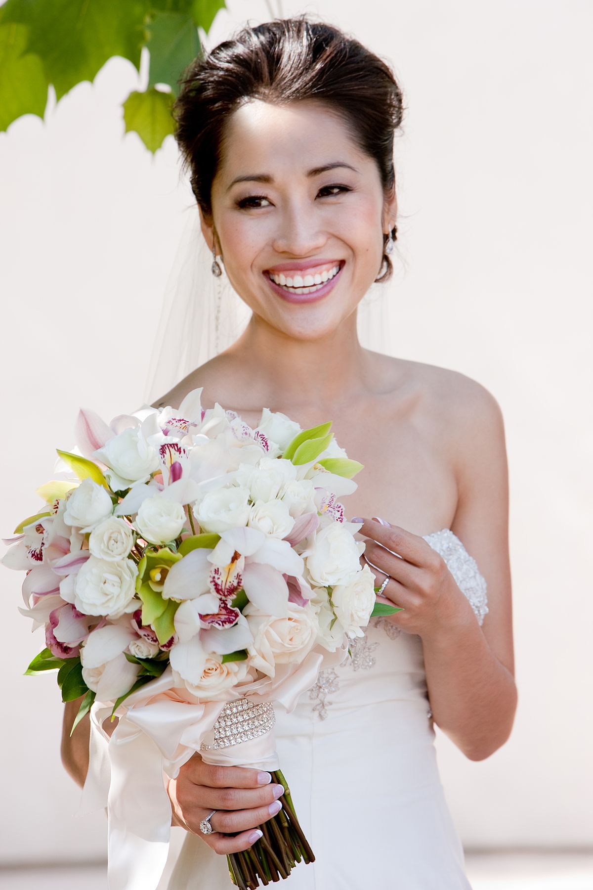 Radiant Asian bride holding a white and pink floral bouquet while smiling on her wedding day.
