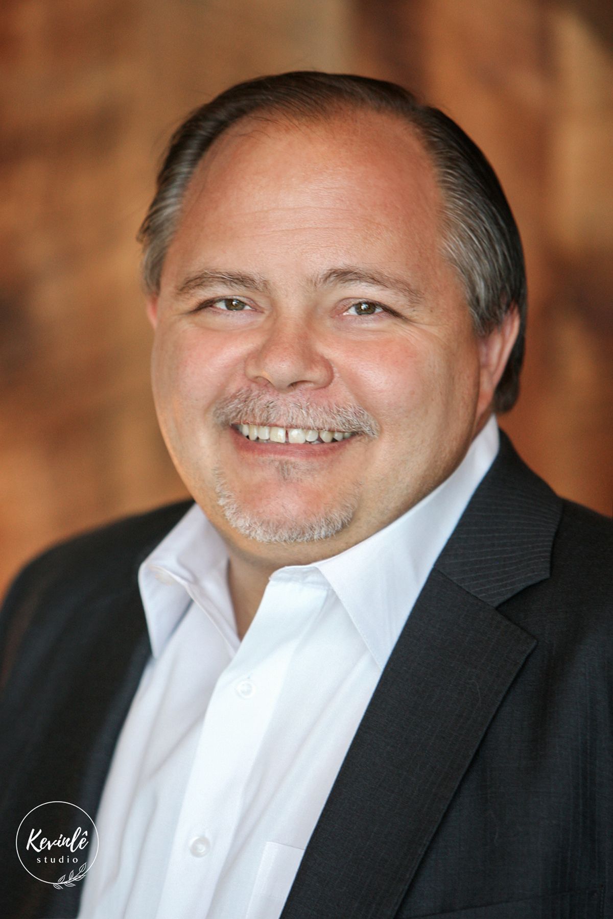 Professional headshot of a smiling middle-aged man in a dark blazer and white shirt.