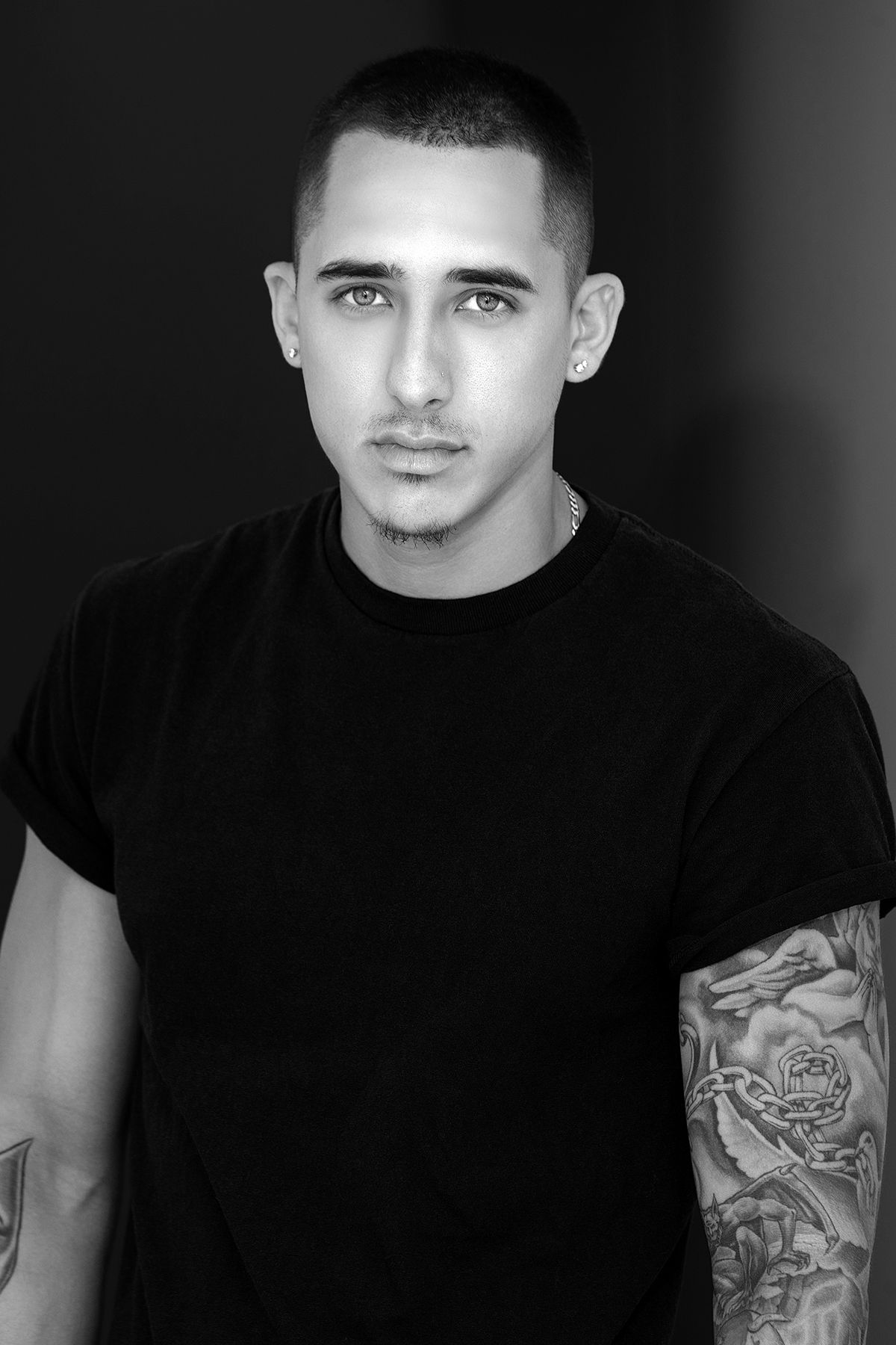 Black and white portrait of a tattooed young man in a black t-shirt with short hair.