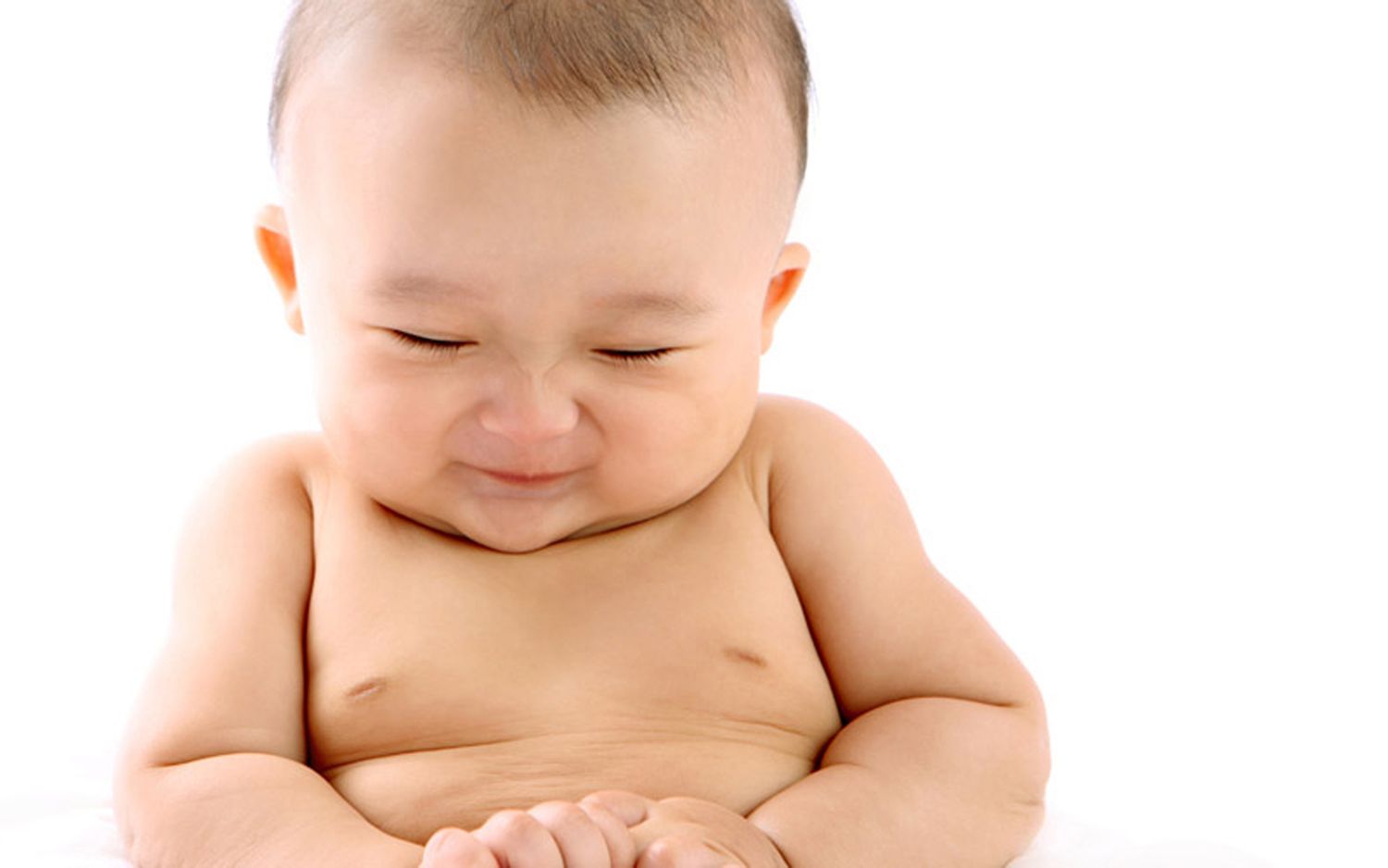 Adorable smiling Asian baby sitting against a white background.