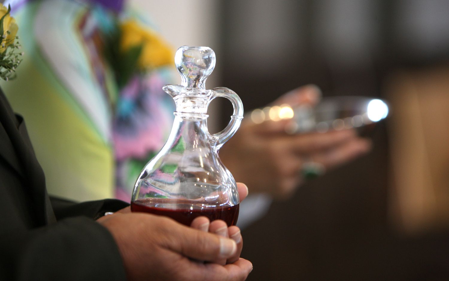 Close-up of hands holding a glass cruet filled with red communion wine during a religious ceremony.