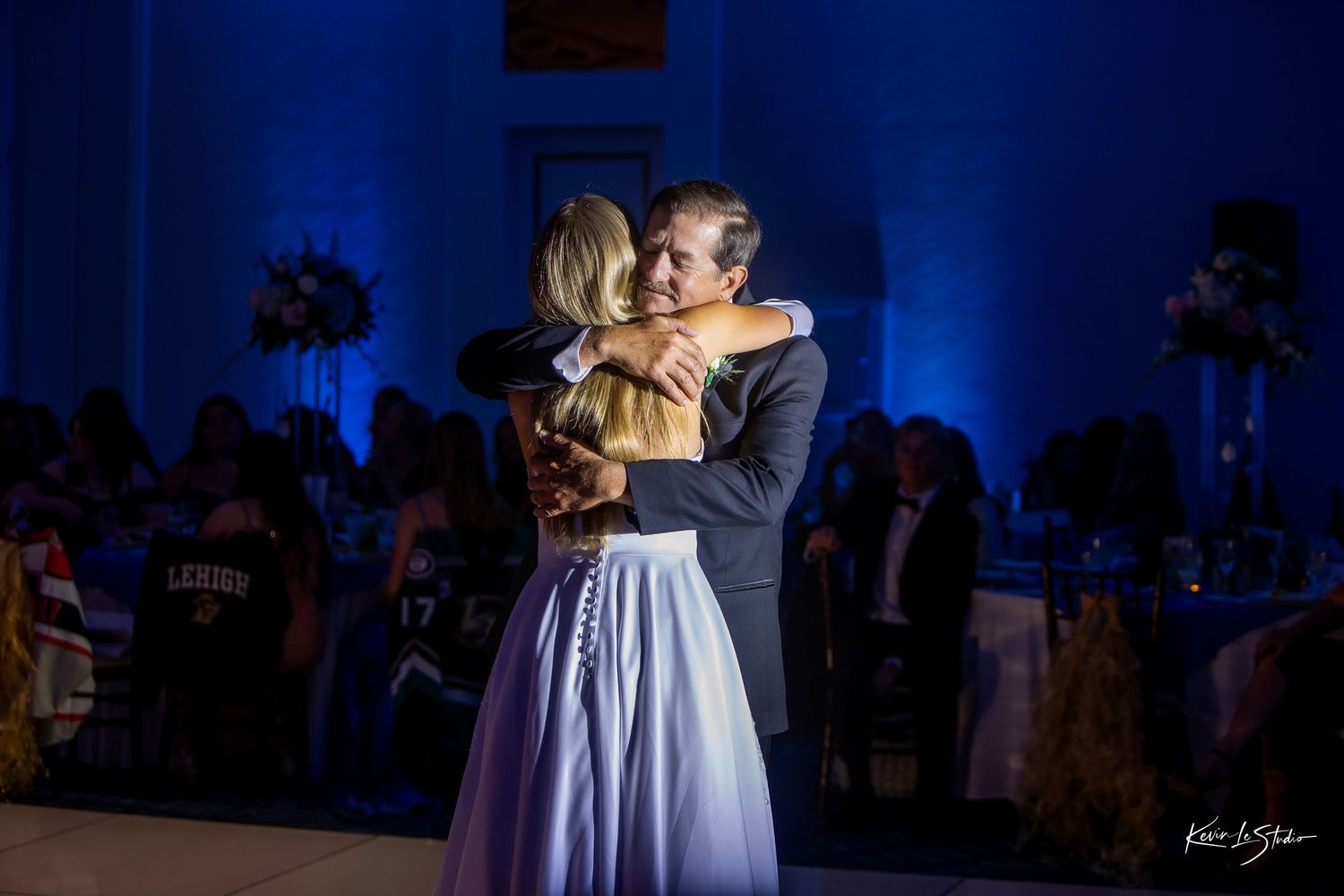 Father and bride share an emotional first dance embrace at a wedding reception with blue uplighting.
