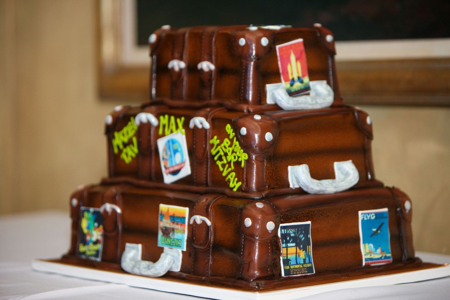 Three-tiered chocolate cake designed as stacked vintage suitcases with travel stickers and name tags for a travel-themed wedding.
