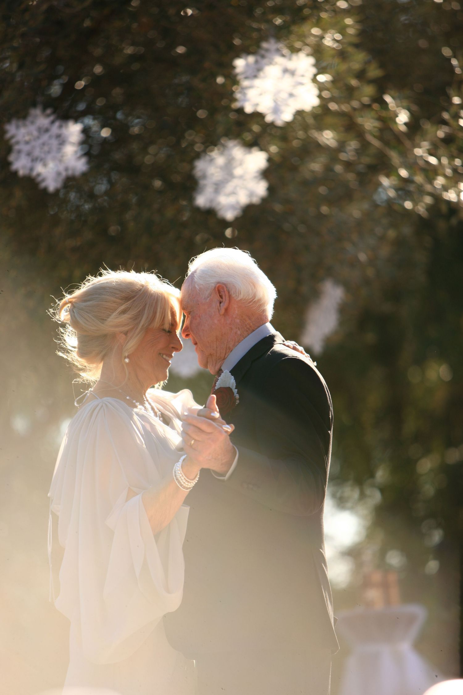 Elderly couple sharing a romantic dance outdoors in golden sunlight, dressed in wedding attire.