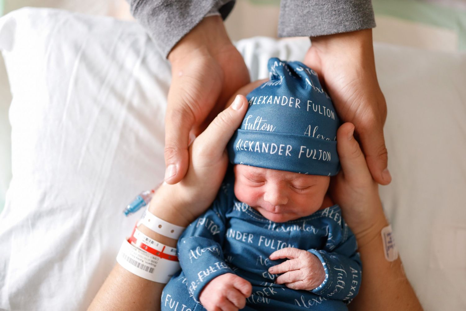 Newborn baby wearing soft blue clothing held in gentle hands.