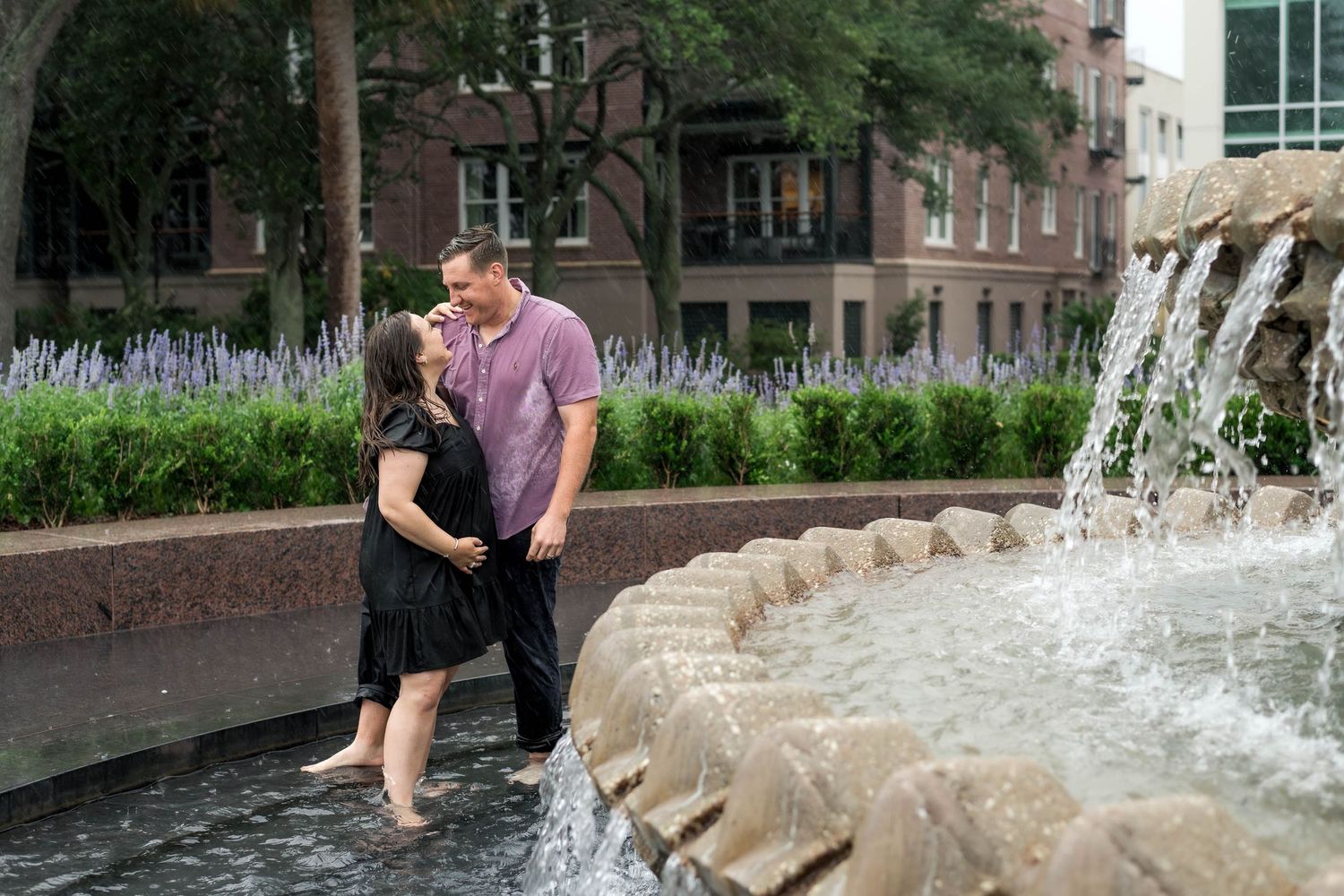 Pineapple Fountain. Couple sharing a tender kiss beside a decorative outdoor fountain during engagement photos.