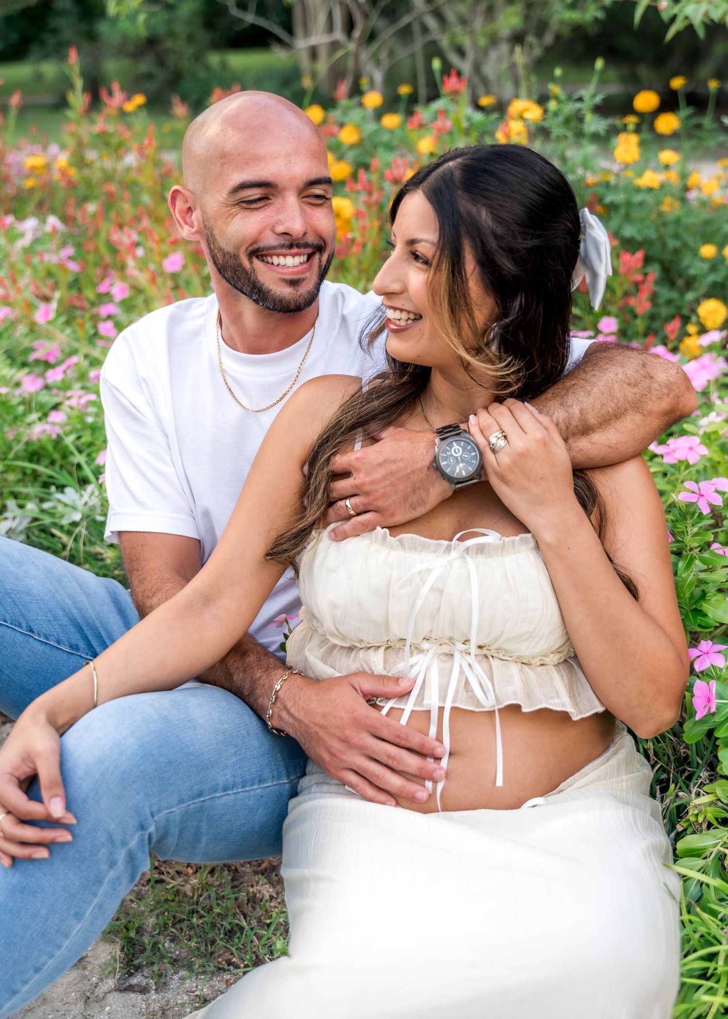 Hampton Park. Smiling couple sitting in colorful flower garden during outdoor maternity photo session.