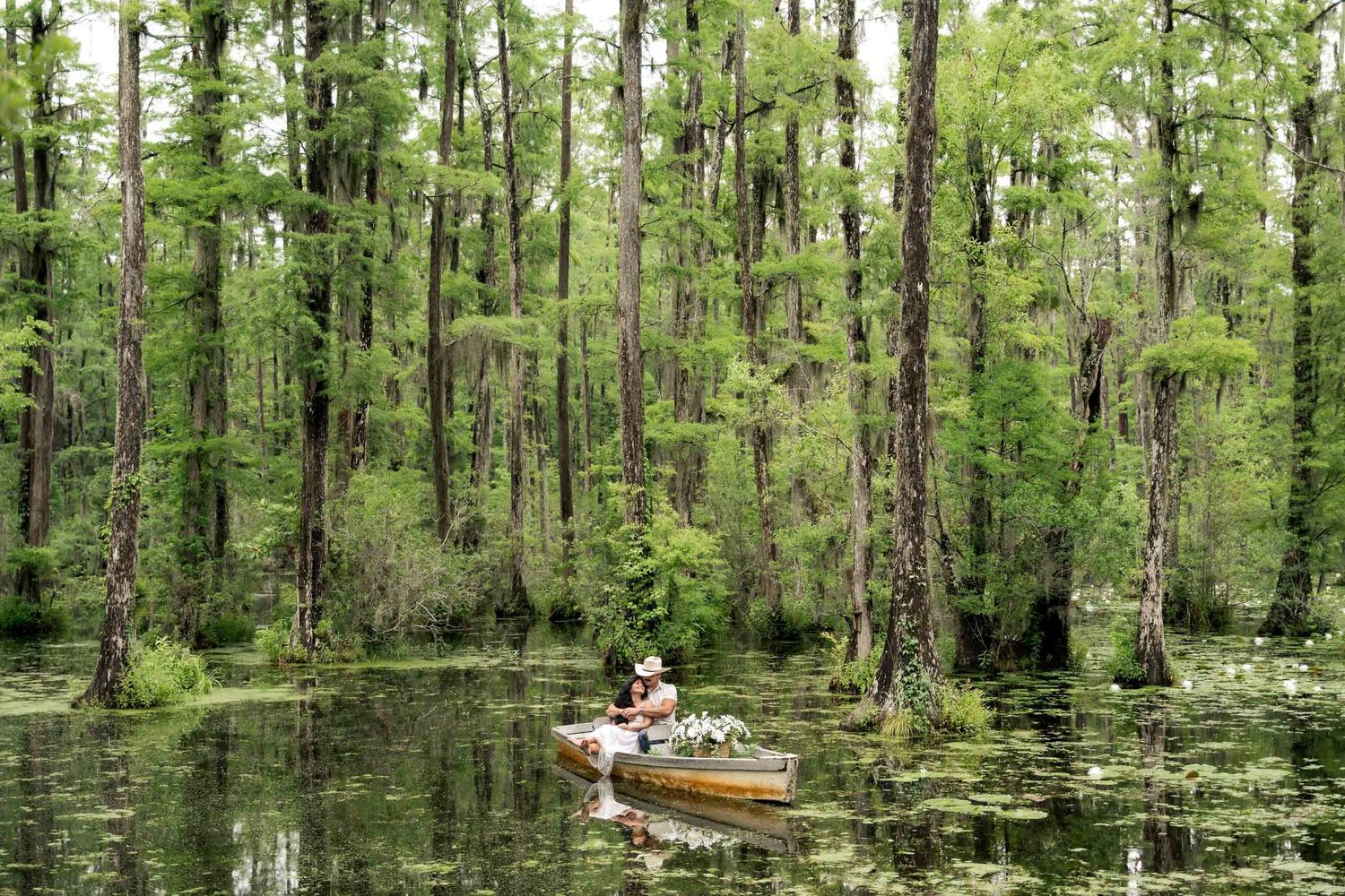 Cypress Gardens. Couple in a rowboat surrounded by tall cypress trees in a lush green swamp.