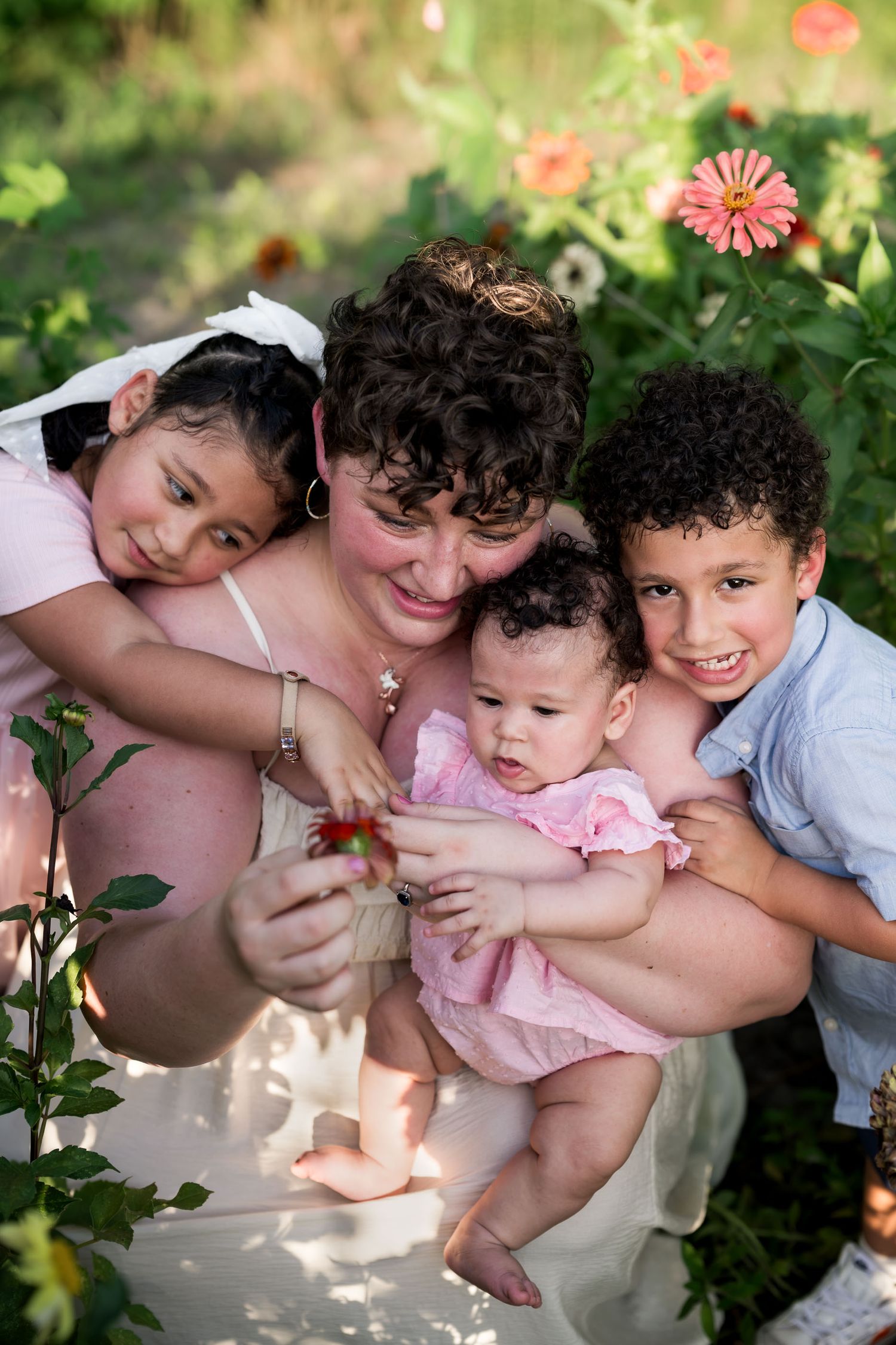 A woman and three children pose together in a garden surrounded by colorful pink zinnia flowers.