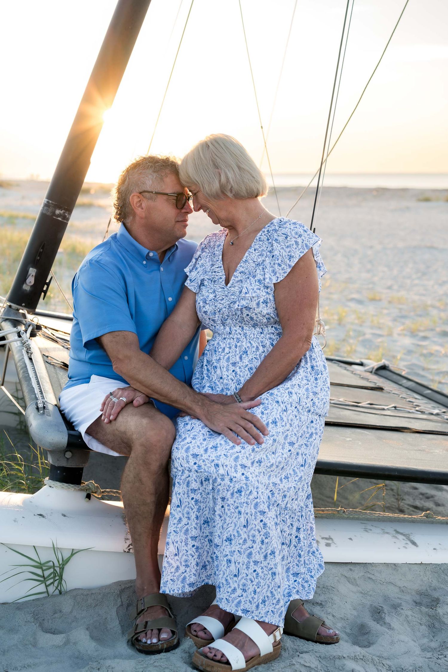 Romantic senior couple sharing an intimate moment on a sailboat at sunset on a sandy beach.